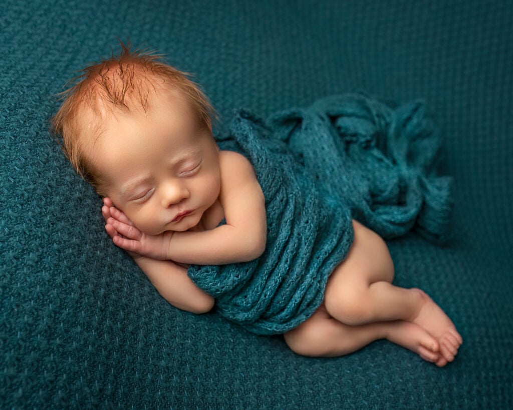 Connecticut newborn photographer baby sleeping in side lying position with red hair on deep teal background