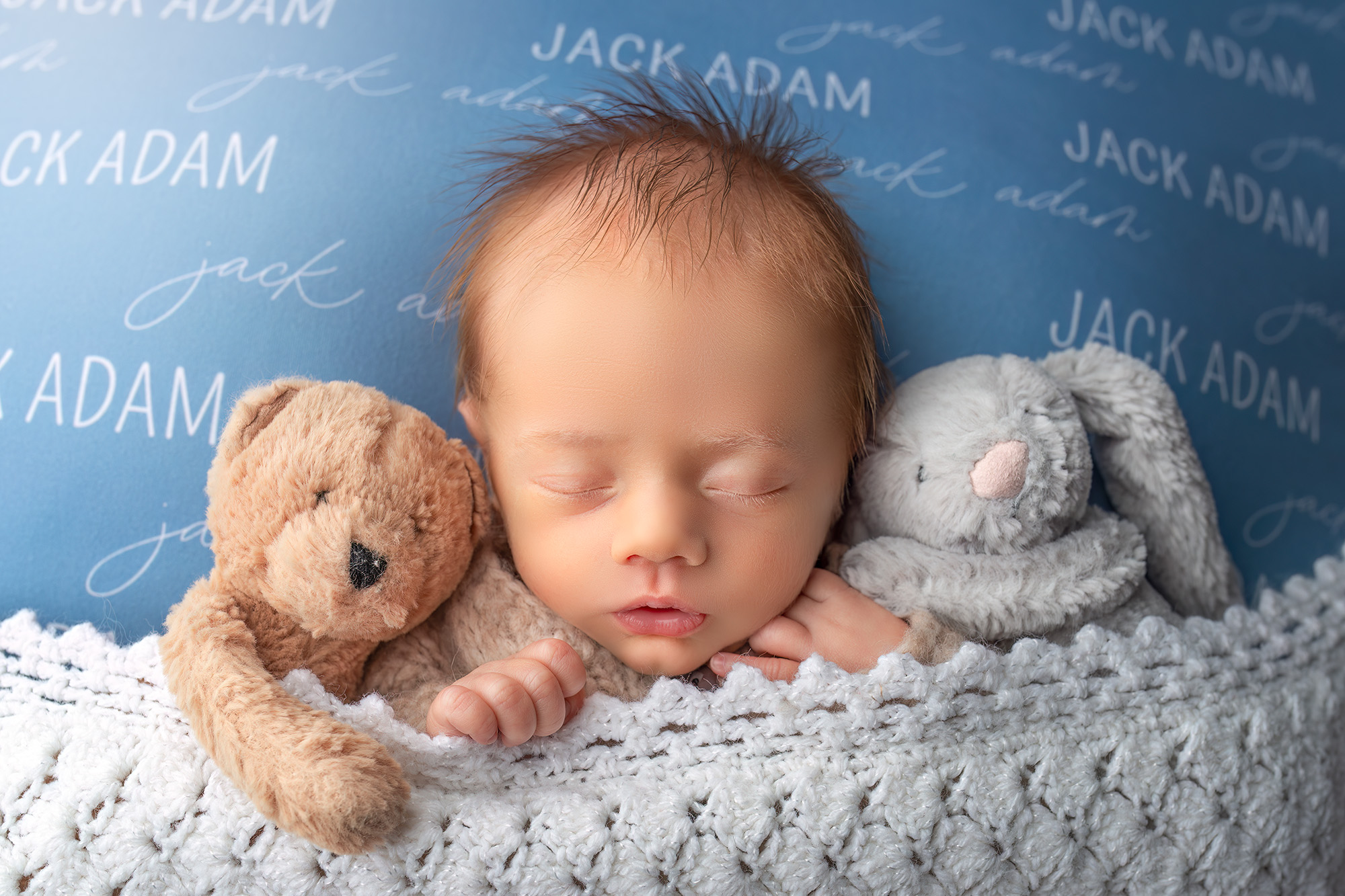 smiling newborn baby fast asleep in between a bear and a bunny on a customized name blanket