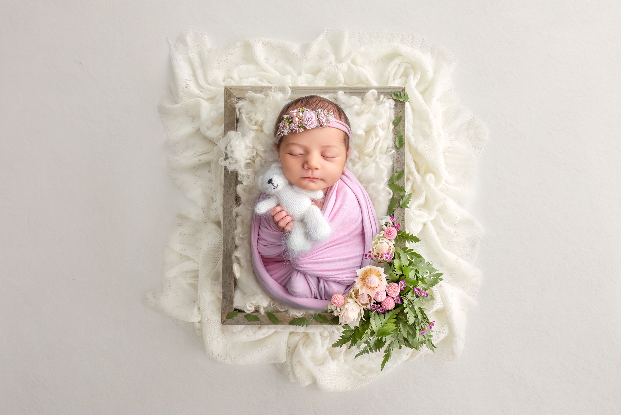 Newborn baby girl laying in a wooden crate with lace behind her and florals beside her