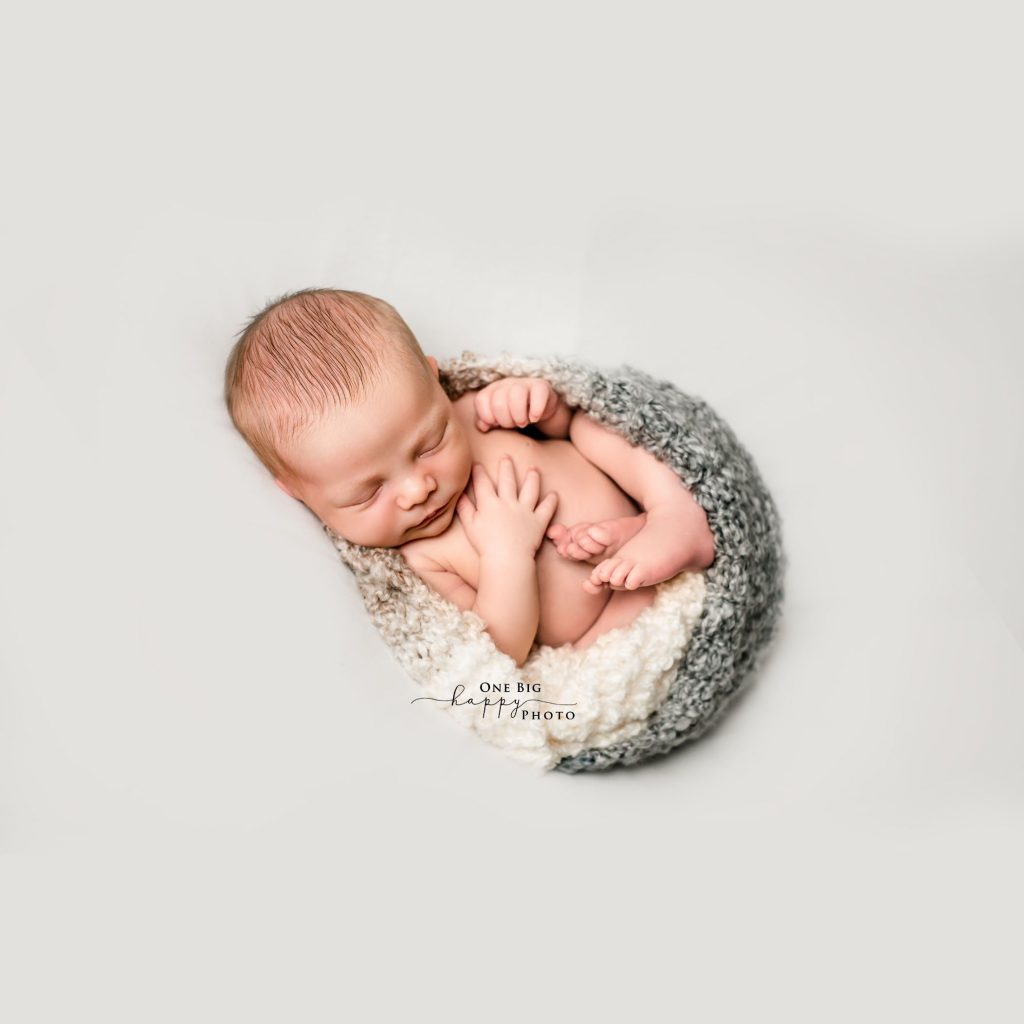 newborn baby wrapped in a fetal position by a knitted blanket