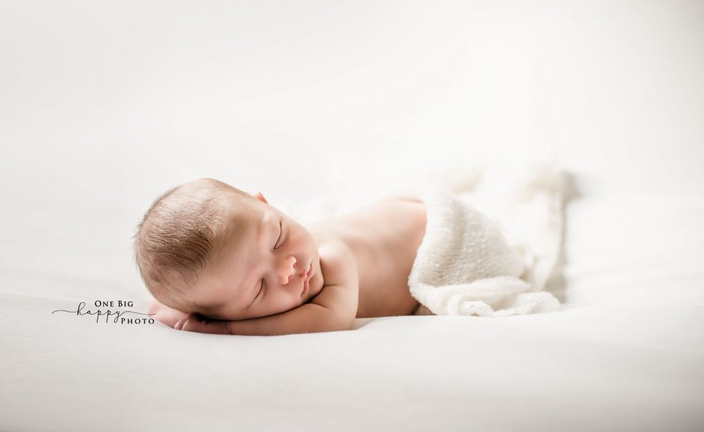 newborn baby sleeping on his tummy on a white background draped in a white wrap