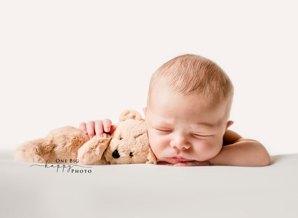 Newborn baby sleeping on his tummy with a teddy bear tucked under his arm