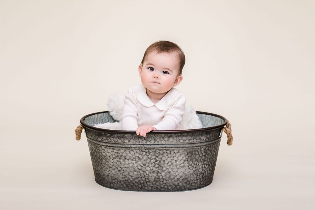 6 month old baby sitting in a rustic tin tub on a cream background