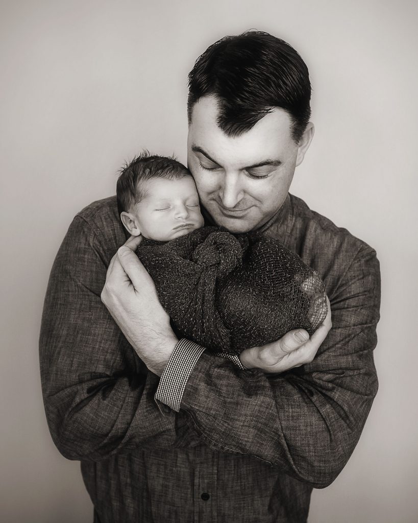 Dad holding his newborn son cuddled up in his arms black and white