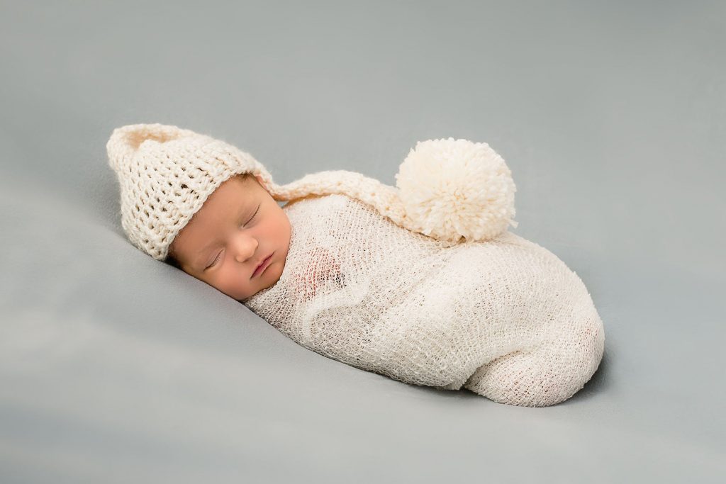 newborn baby wrapped in cream wrap with long knitted cap and pompom