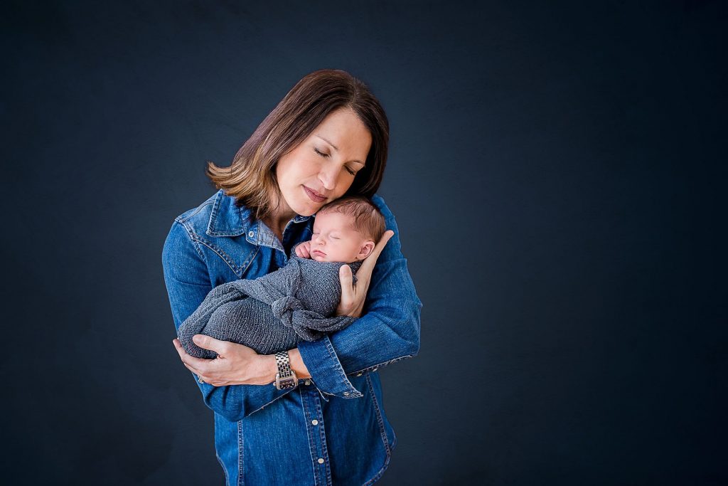 Mom snuggles newborn on blue background with blue denim shirt