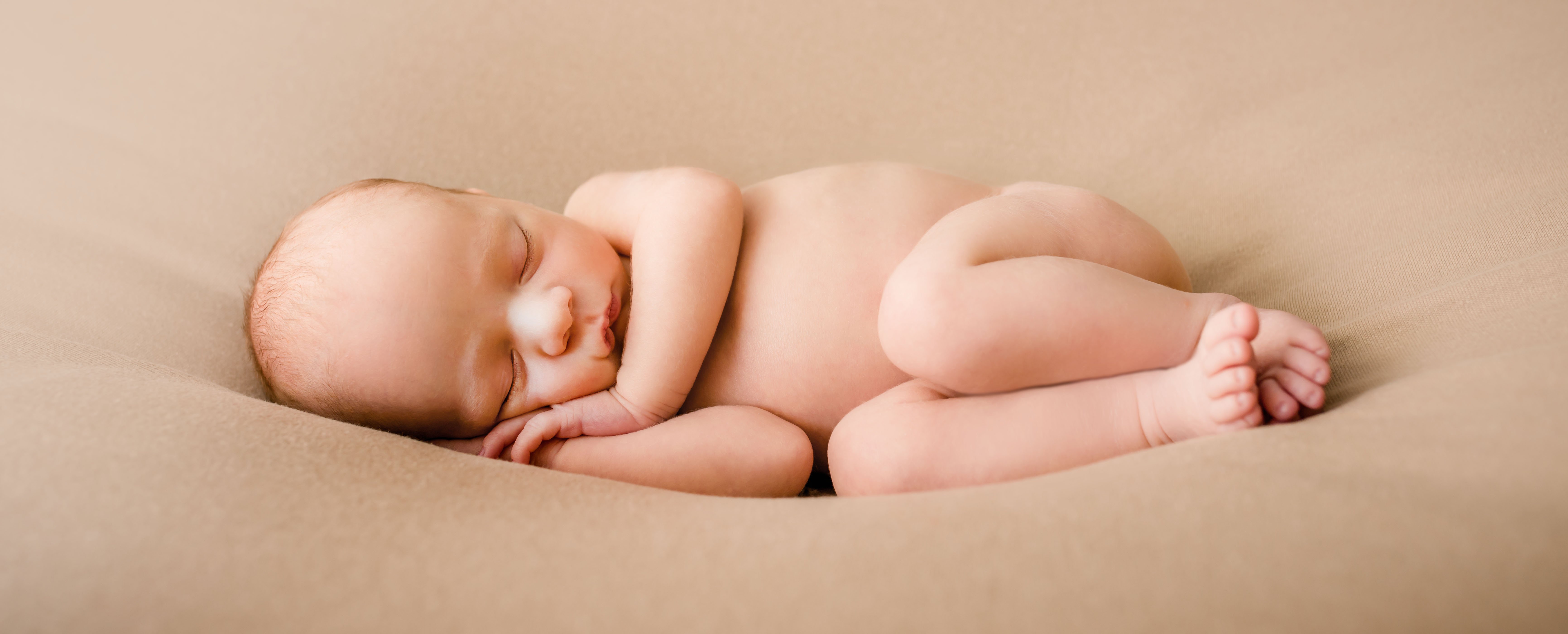 newborn baby boy sleeping on his side on tan blanket