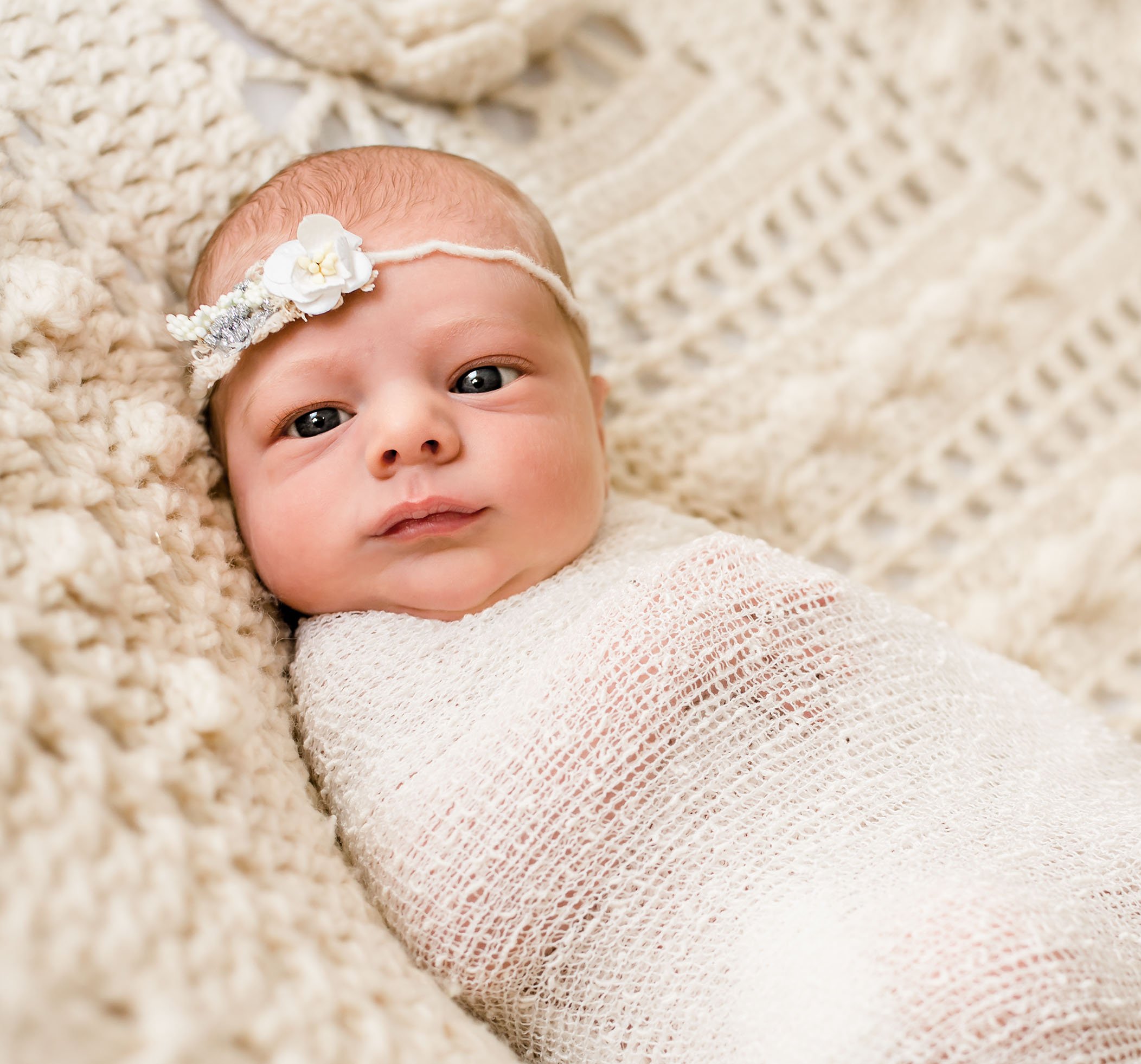 newborn baby girl wrapped in cream with a flower headband