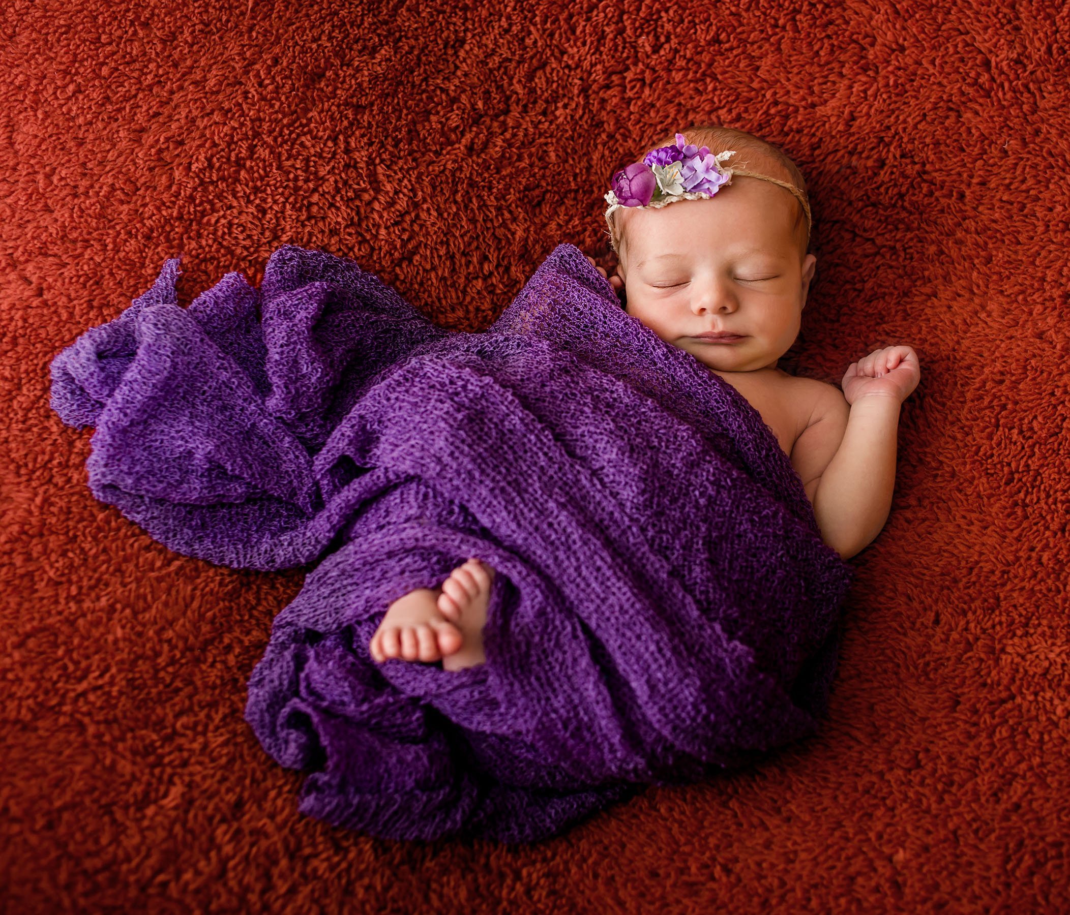 newborn baby girl wrapped in deep purple on an red blanket