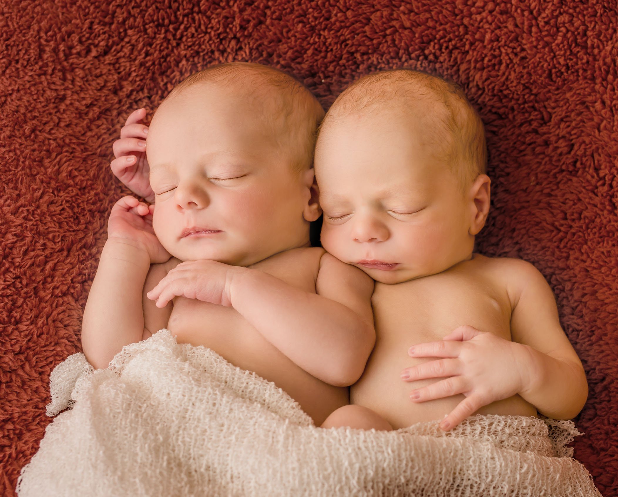 newborn twins sleeping with a cream blanket on them while lying on an orange blanket