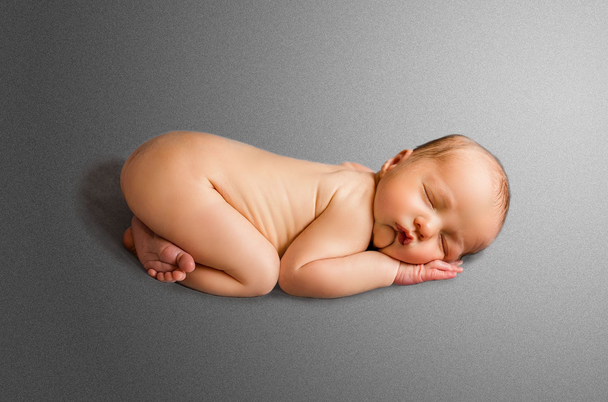 newborn baby lying on tummy in bum-up pose with grey background