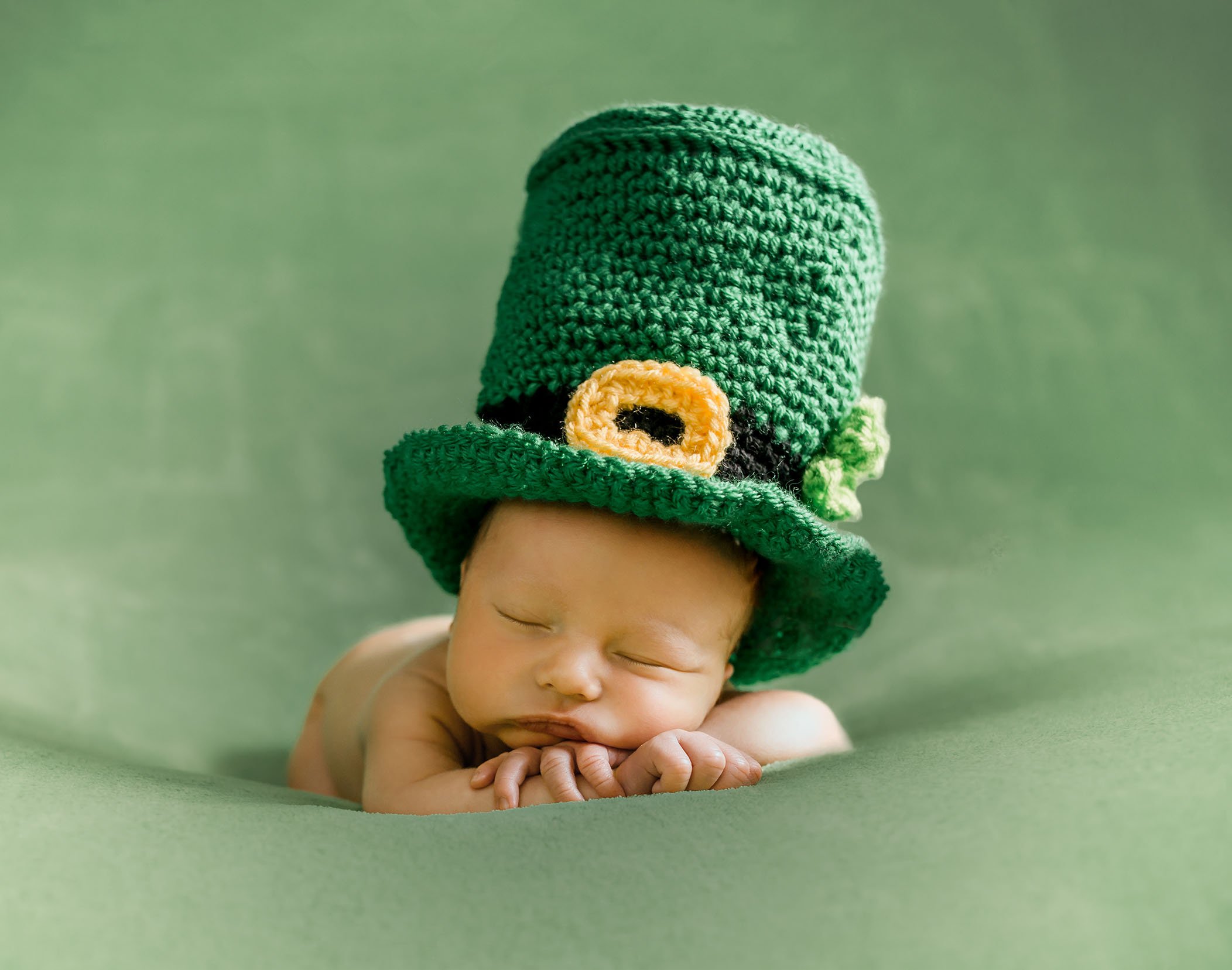 newborn baby on a green background with a leprechaun top hat on