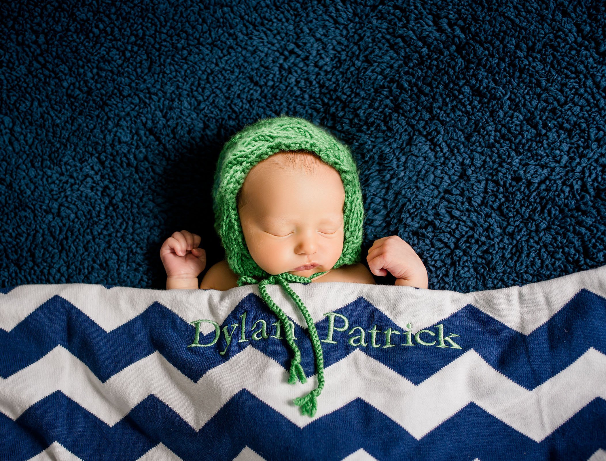 newborn baby boy tucked in for sleep in a green bonnet on blue background