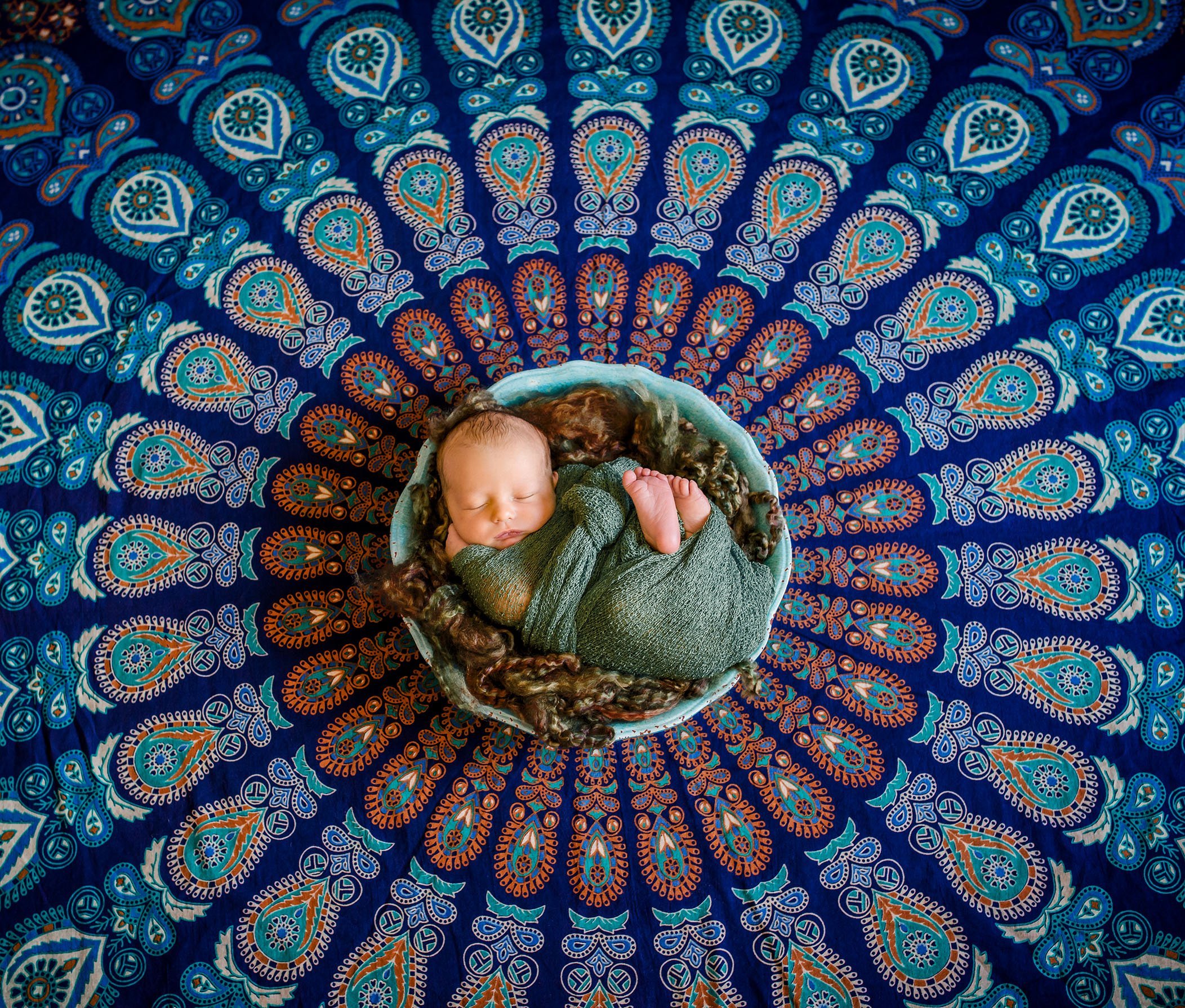 newborn baby curled up in a bowl in the middle of an Indian spiral tapestry
