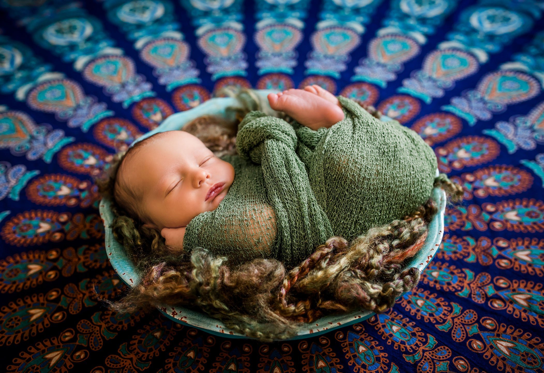newborn baby curled up in a bowl with green wrap on colorful background