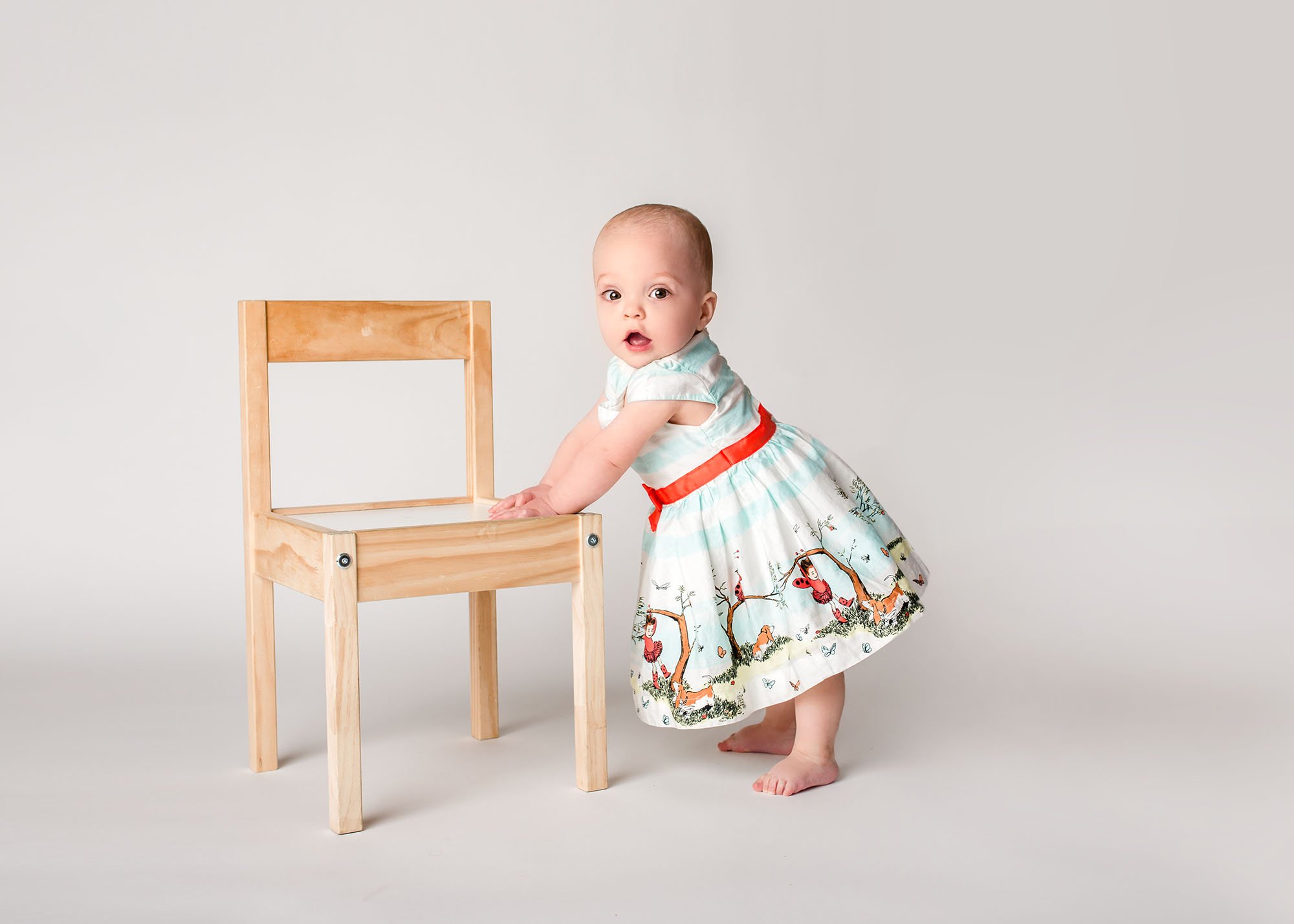 one year old baby girl in ladybug dress standing up holding onto a chair Glastonbury CT Baby Photographer One Big Happy Photo www.onebighappyphoto.com/babies