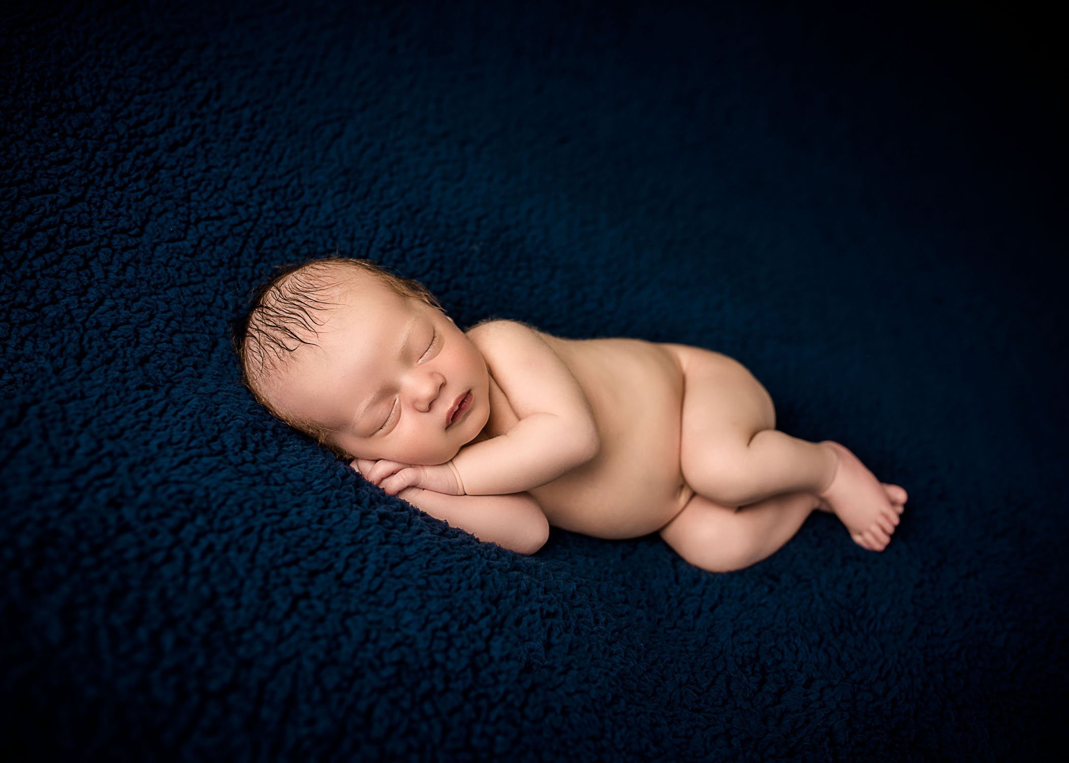 newborn baby boy sleeping on his side on dark blue blanket
