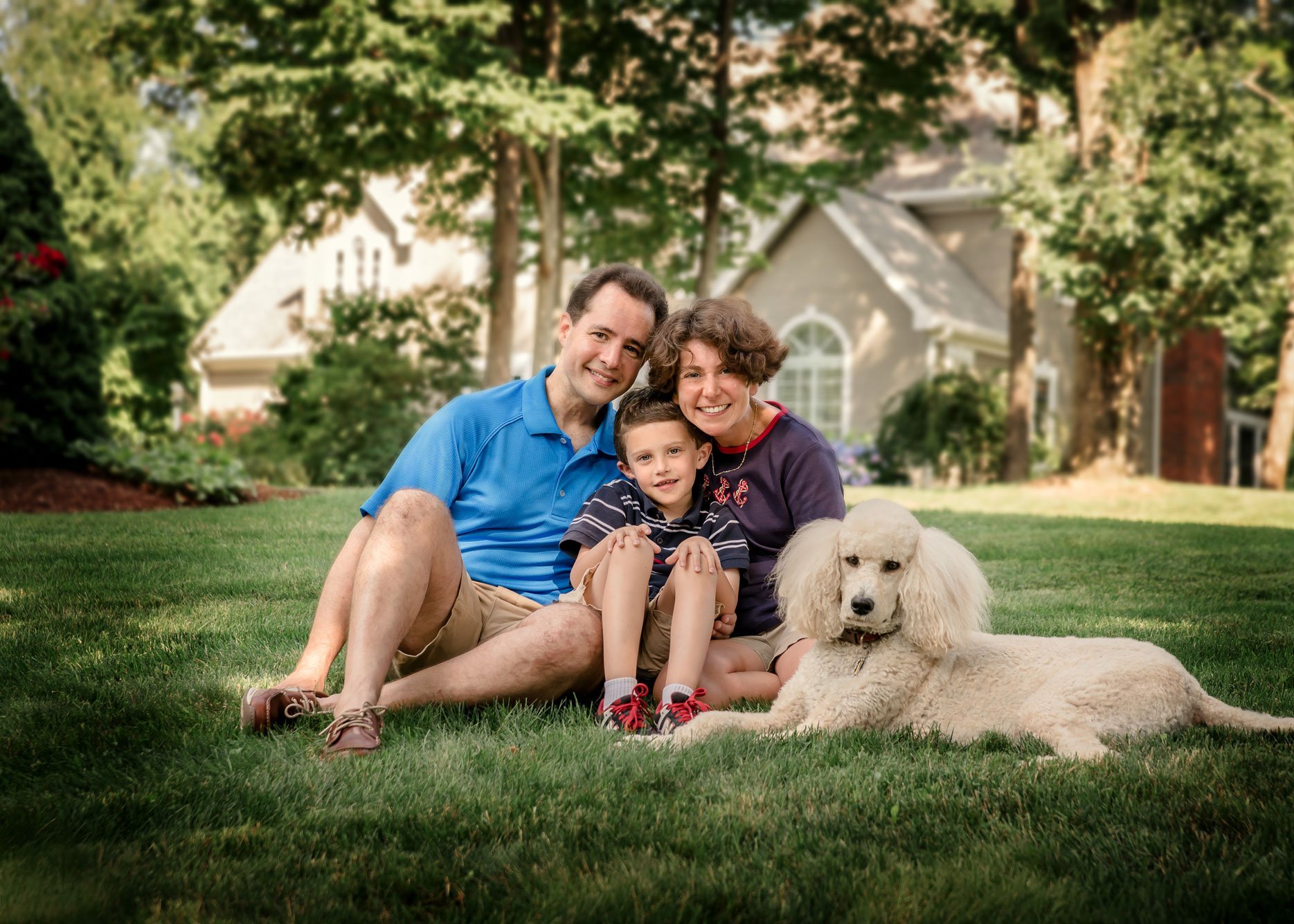 Dad, Mom and young son pose for family portrait with giant white poodle in front yard