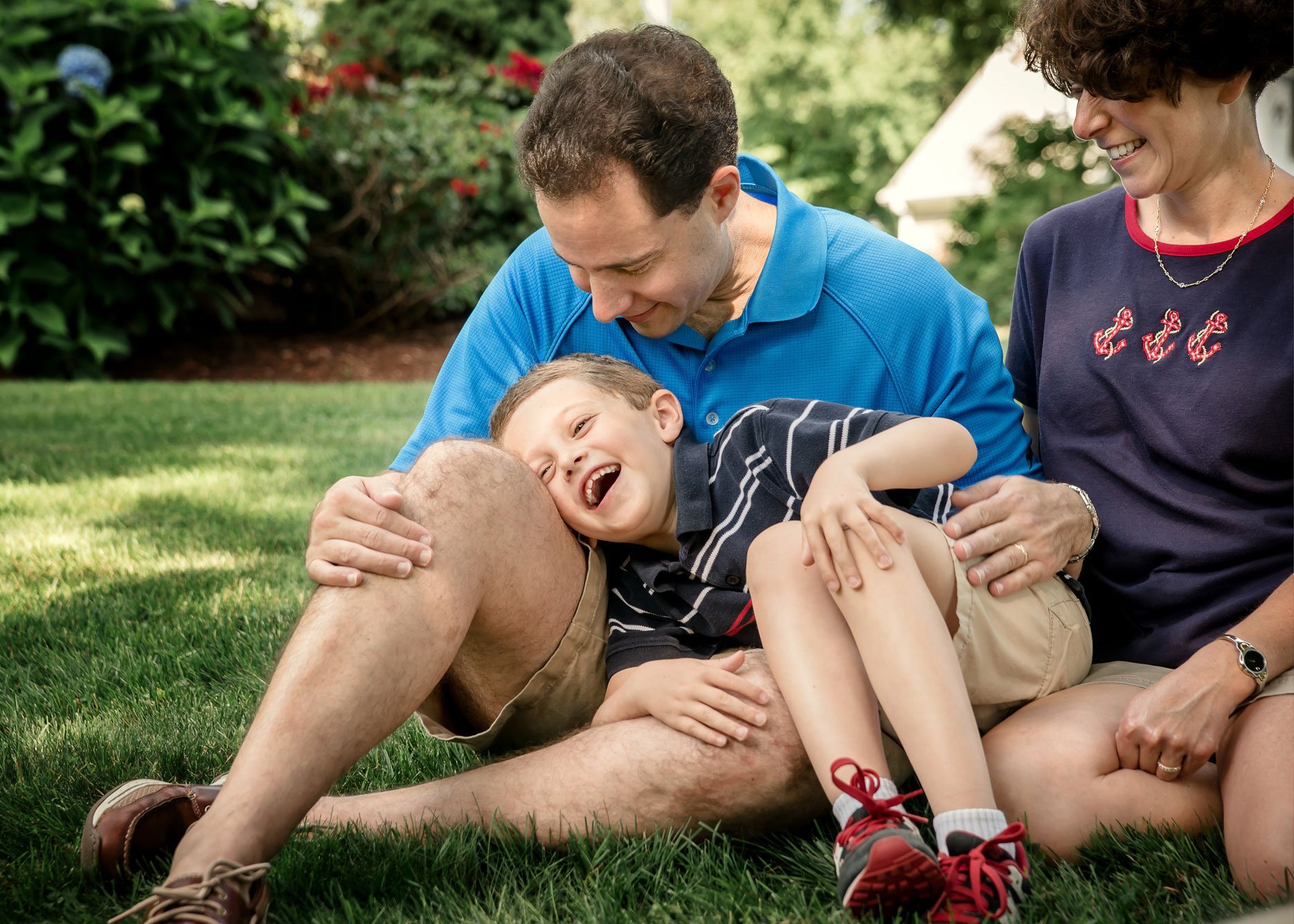 young son laughing on Dad's lap outside in summer