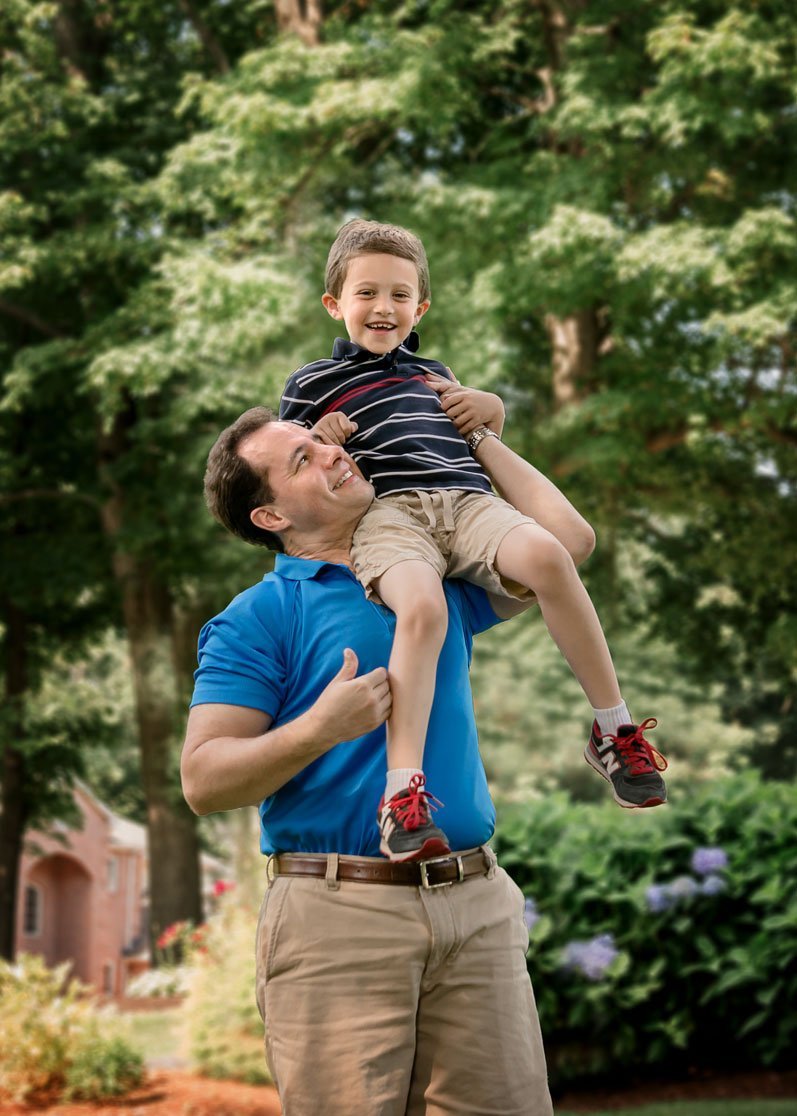 young son rides on Dad's shoulders outisde in summer