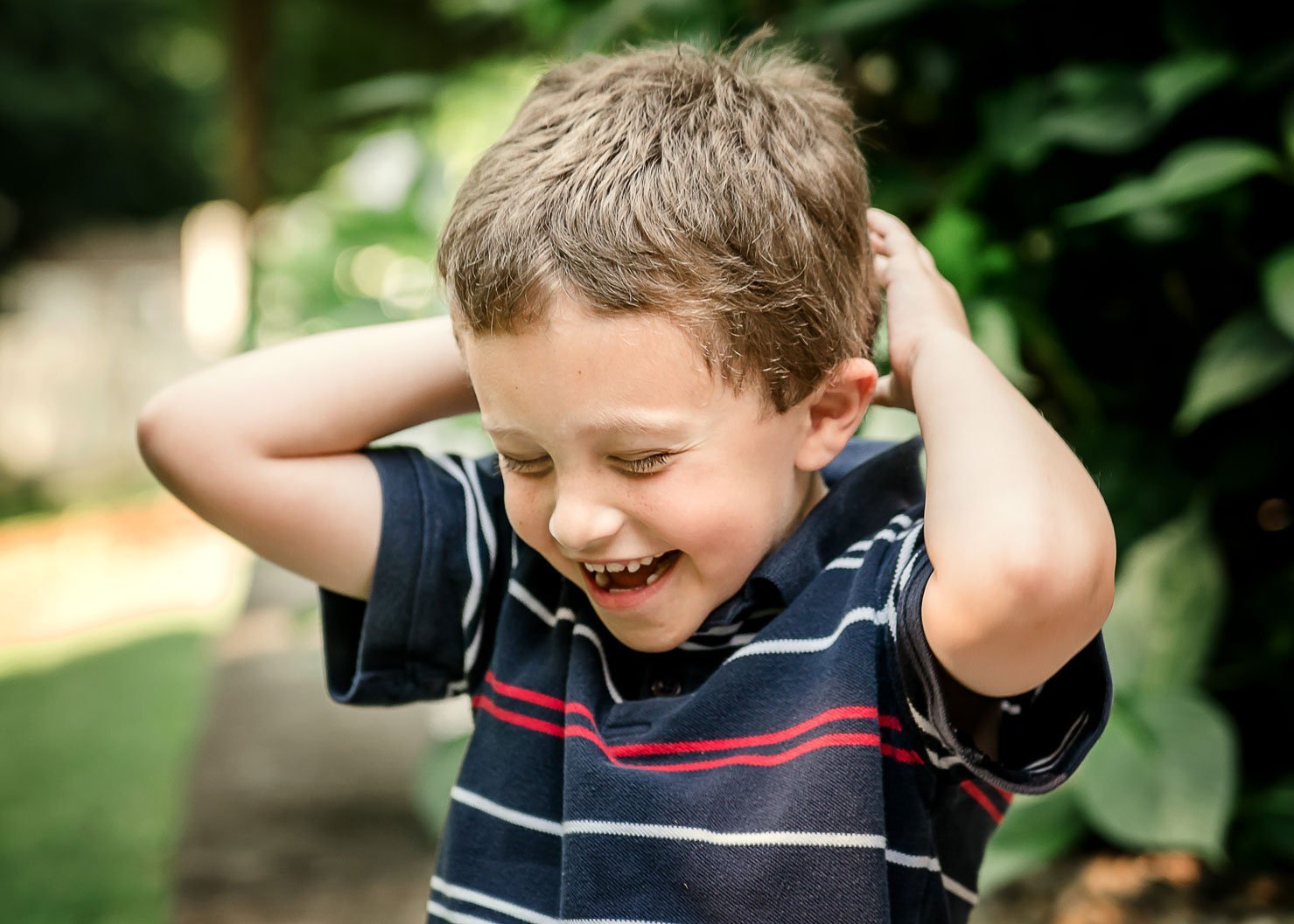 young boy laughing with eyes closed outside in summertime