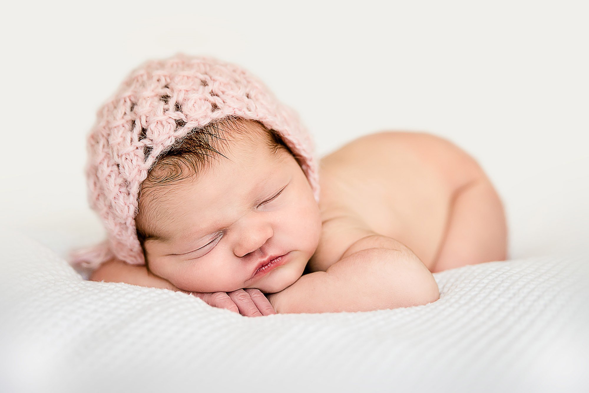 Newborn baby girl sleeping with head on hands with a pink knit cap on