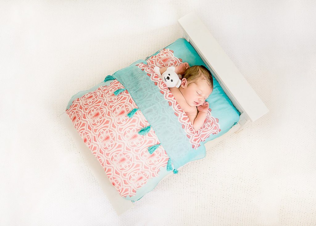 Newborn baby sleeping in a doll bed with a teddy bear