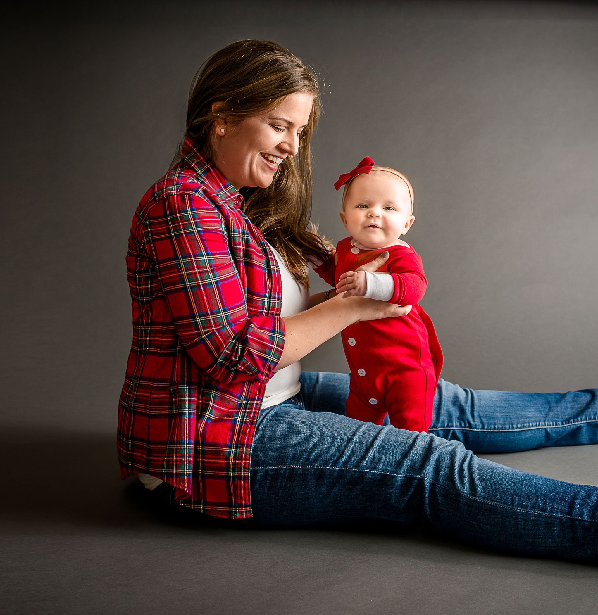 Mom holding 6 mo old baby girl standing up in red pajamas One Big Happy Photo