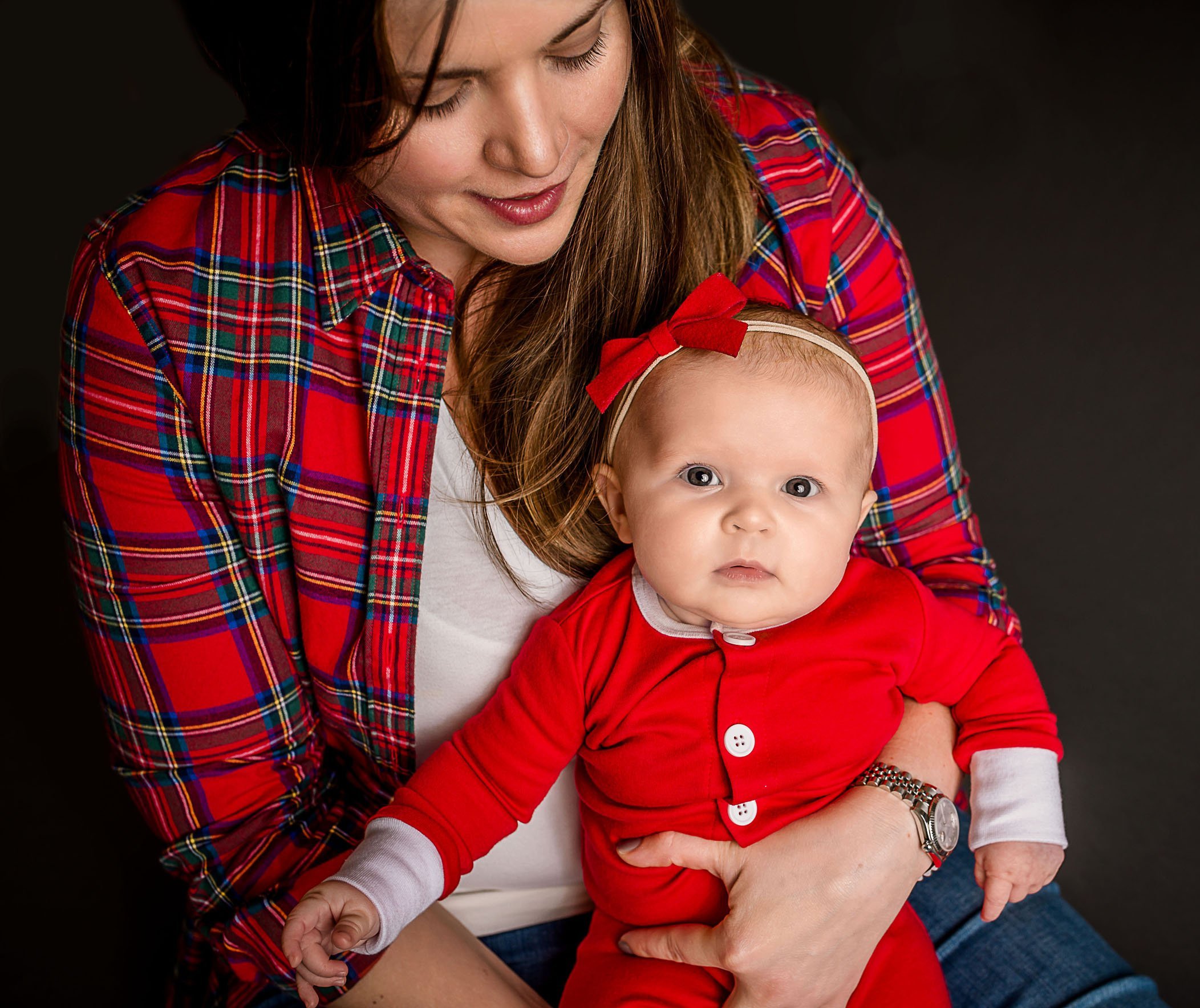 Mom holds 6 mo old baby girl in red pajamas with bow One Big Happy Photo