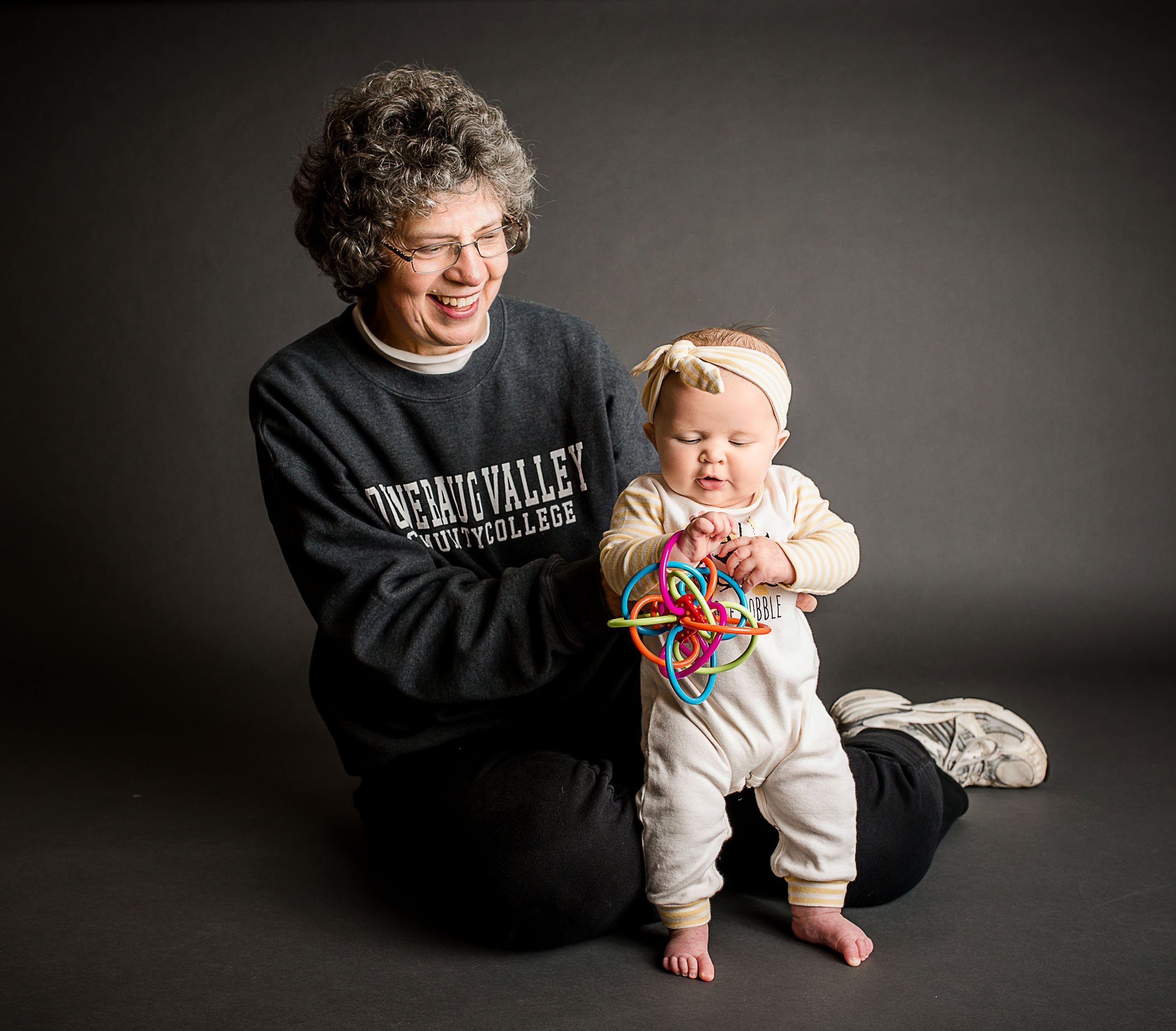 Grandma holding 6 mo old baby standing and playing with a toy One Big Happy Photo