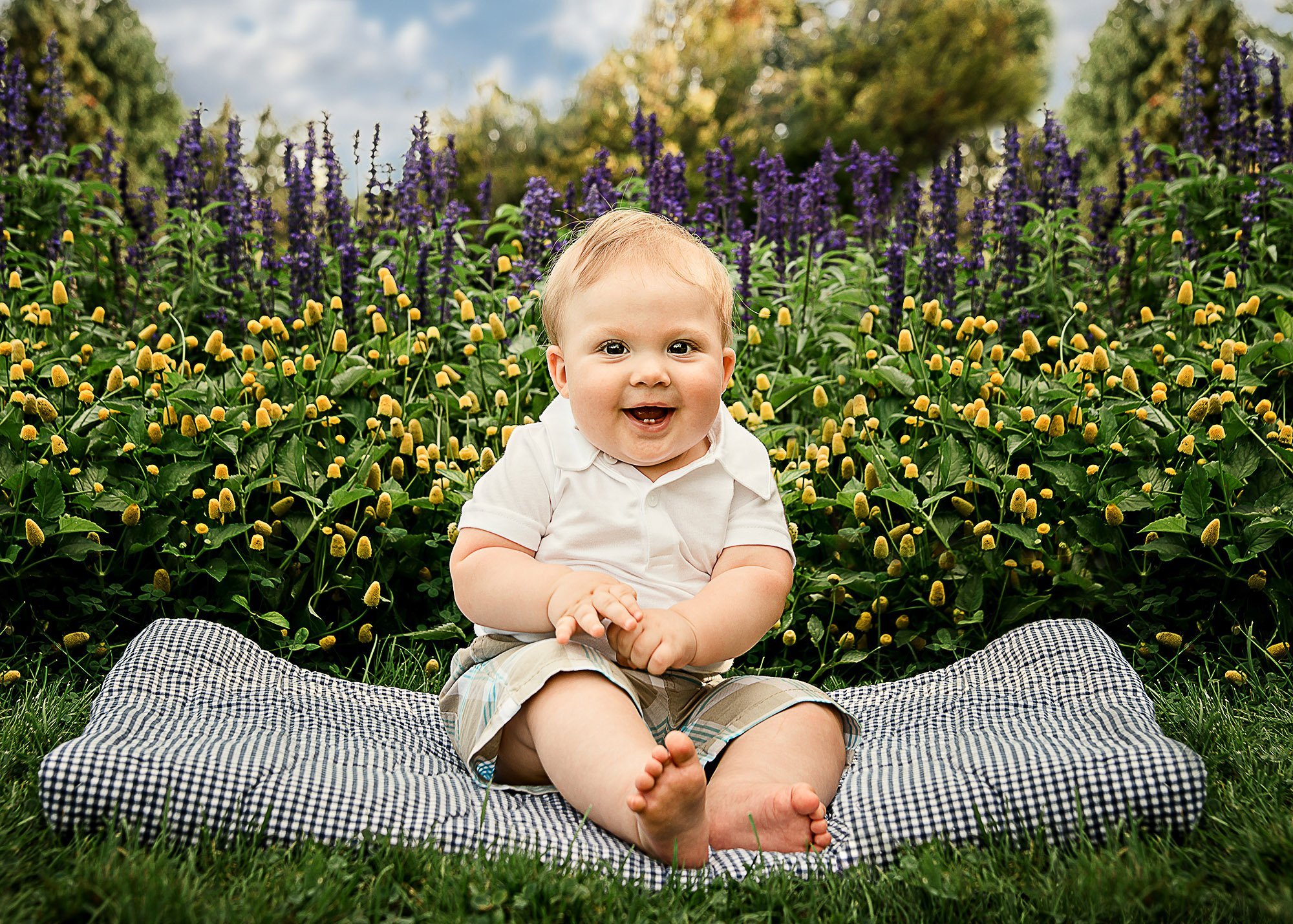 Joyful 6 month old boy sitting up in the garden with a big smile