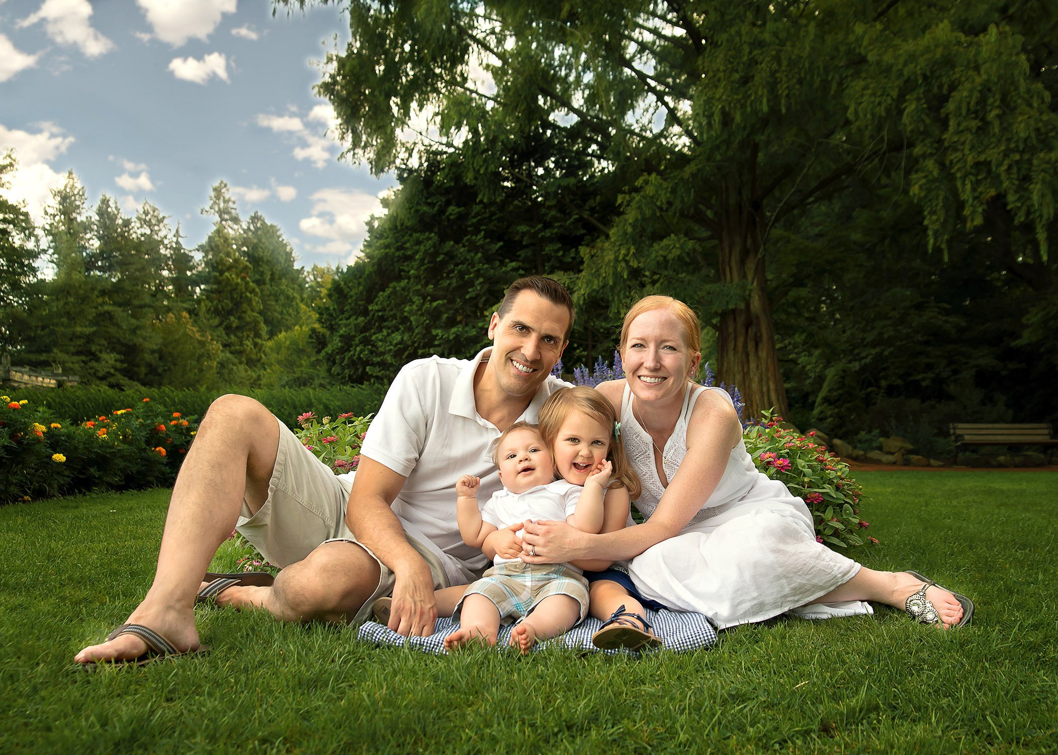 family of 4 sitting in the garden in the summer smiling for a portrait