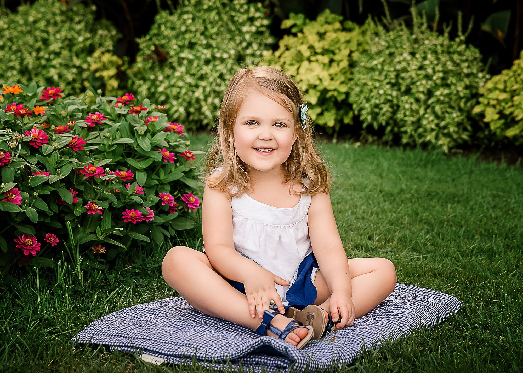 3 year old girl sitting for a portrait on a blue blanket in the garden