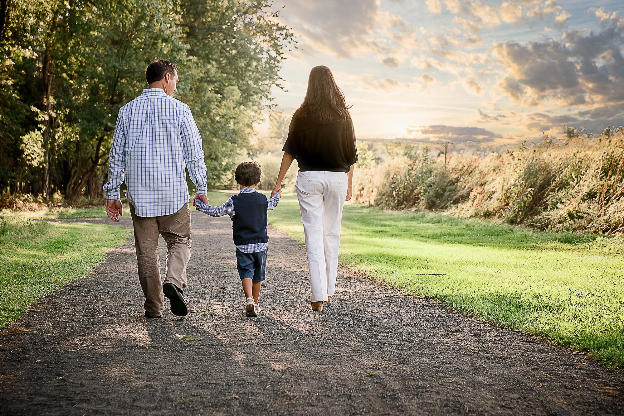 Mom, Dad and young son walking on a road at sunset