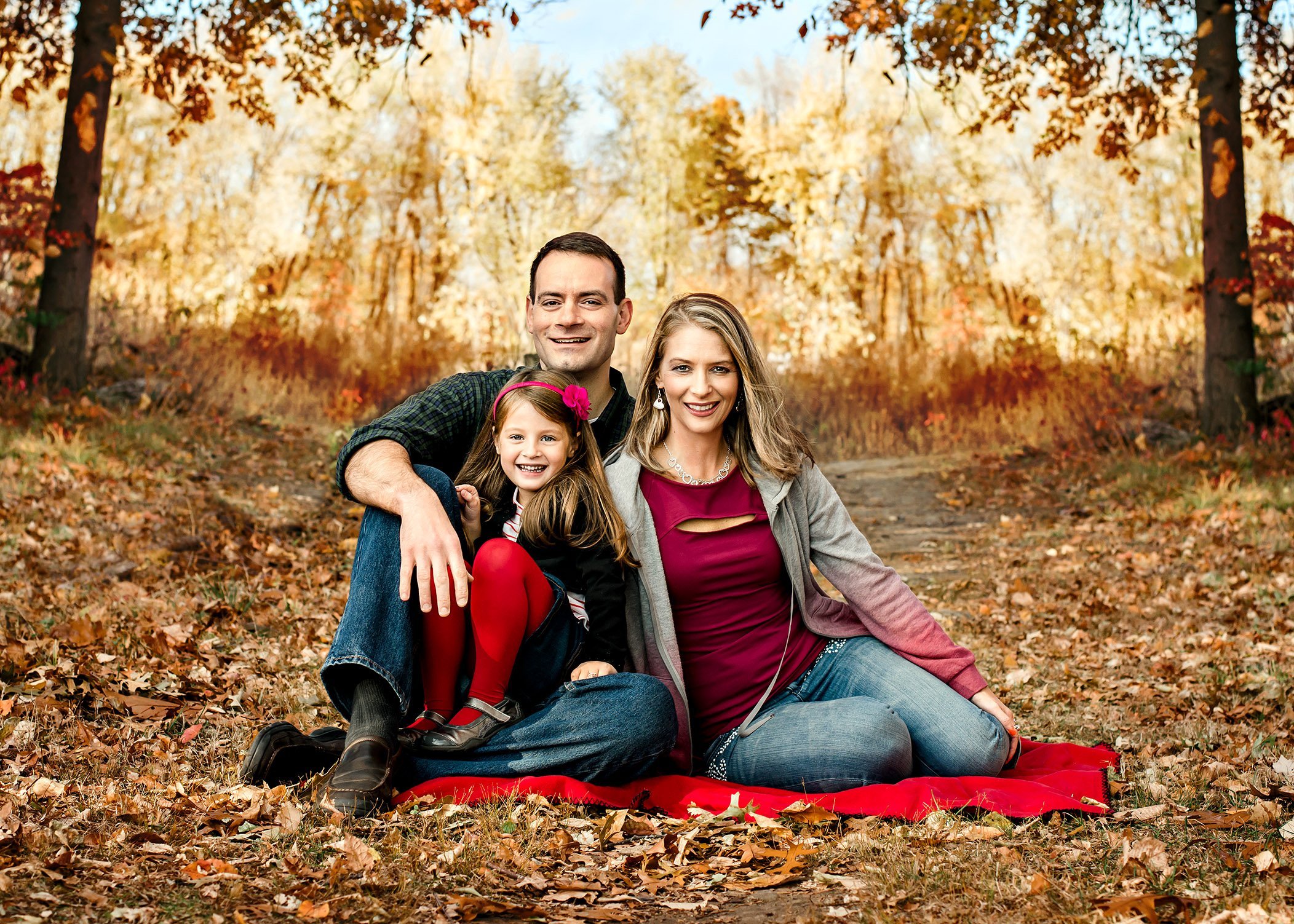Family of 3 pose for a family portrait outside in the fall leaves