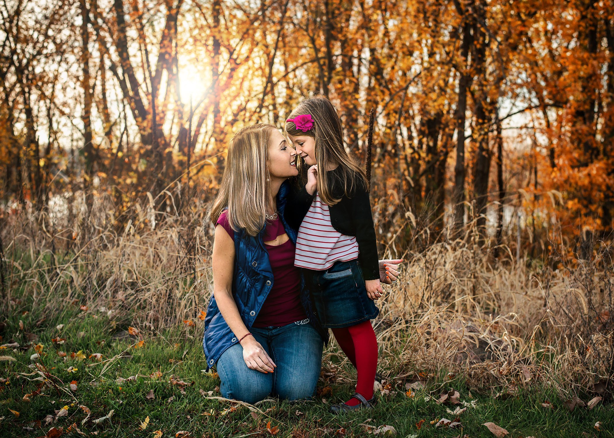 Mom and young daughter exchange nose kisses at sunset in the fall