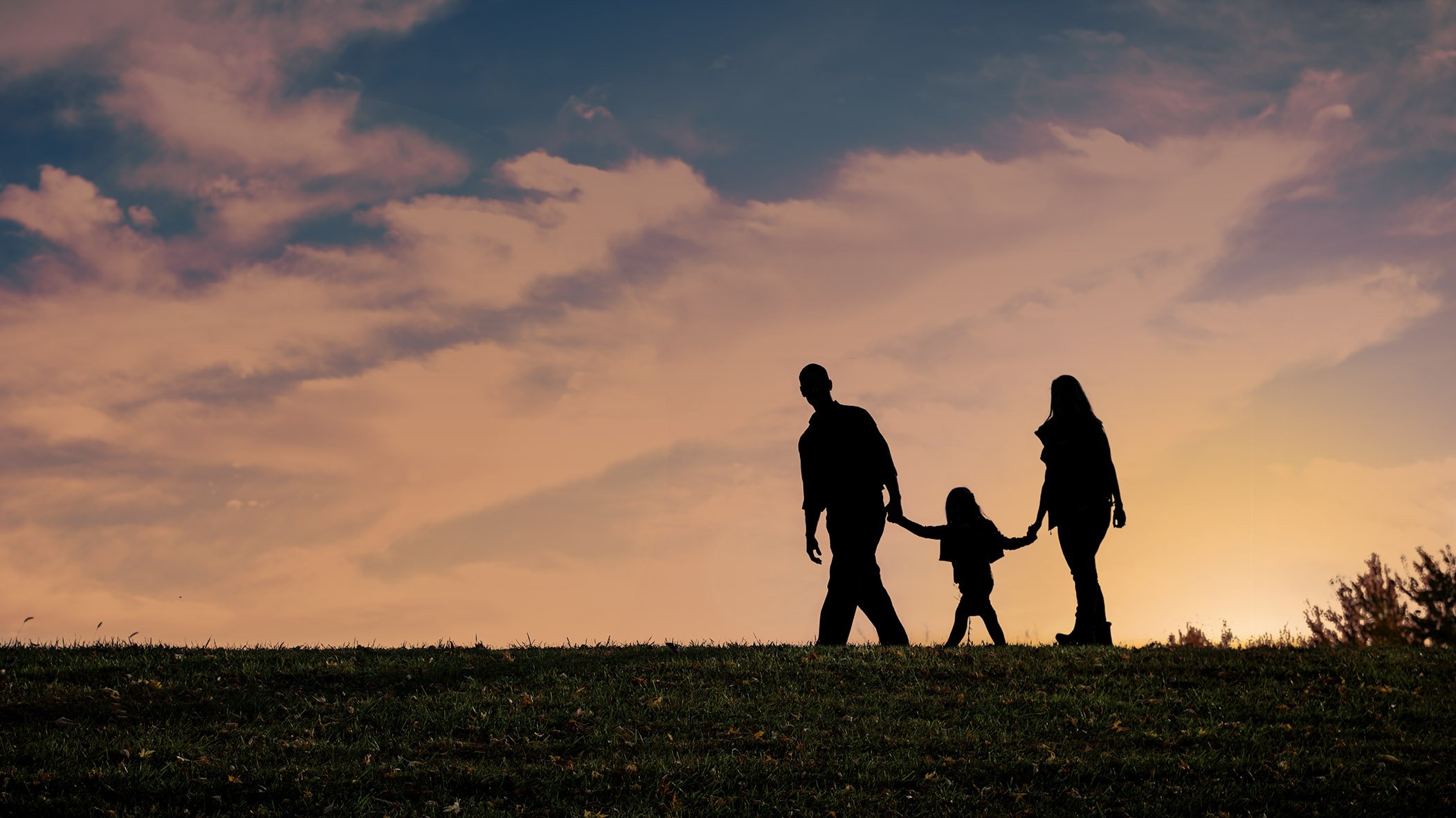 Mom, Dad and young daughter walking at sunset with orange and blue sky
