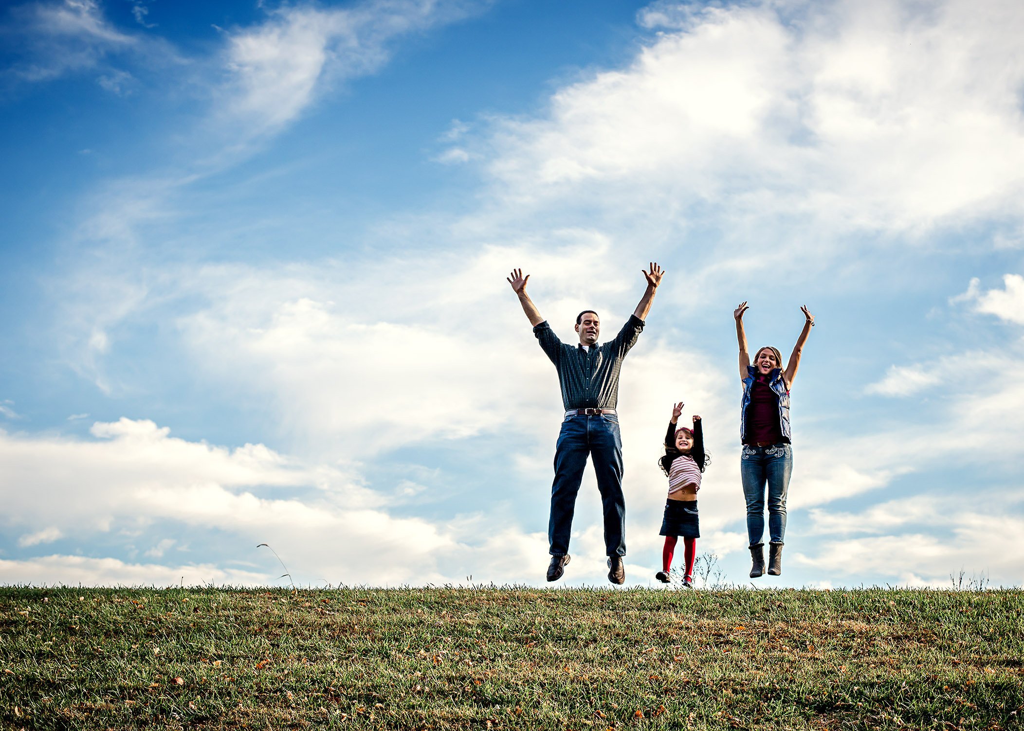 Mom, Dad and young daughter jump in the air outside at the same time