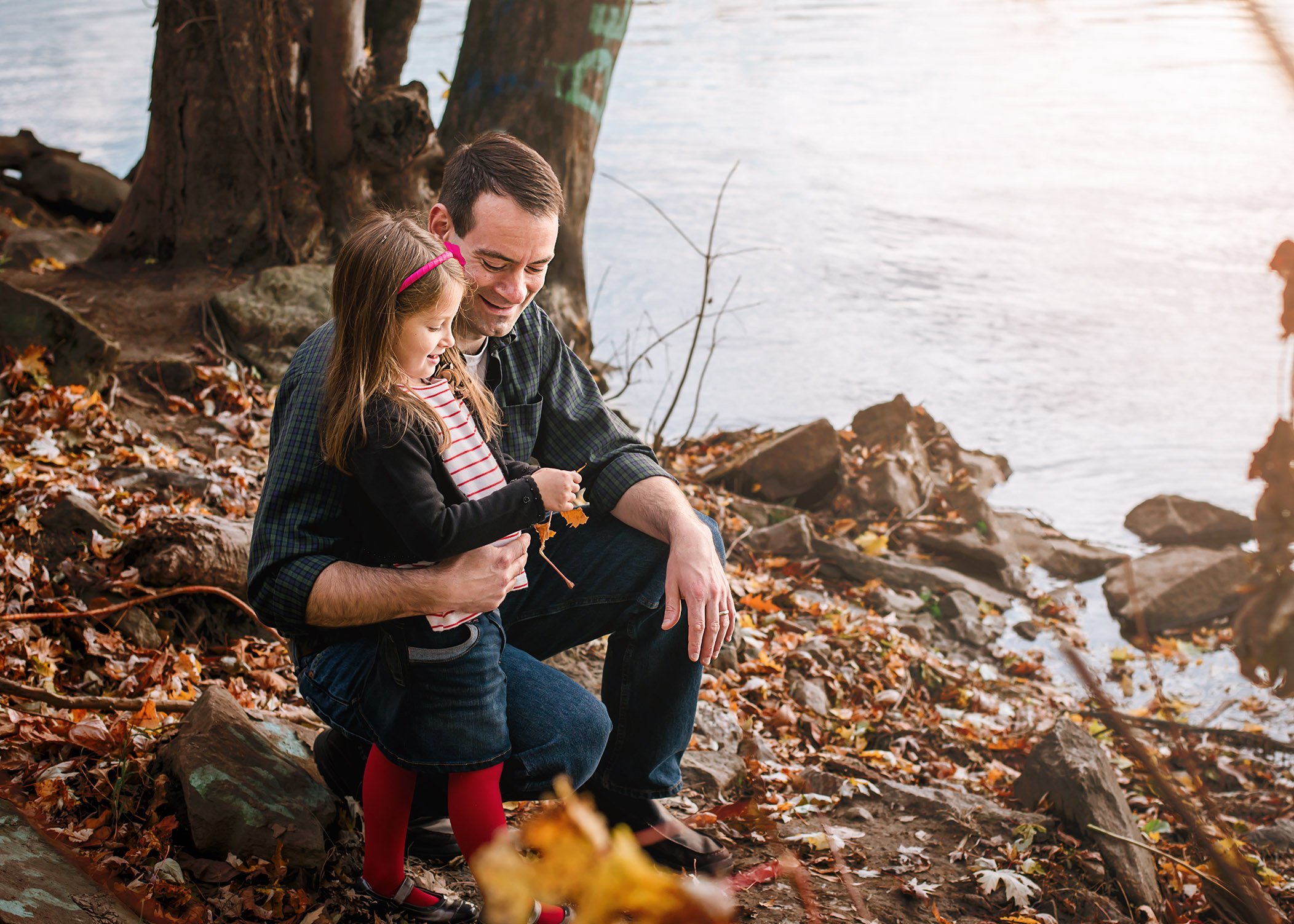 Dad and young daughter looking at fall leaves by the river