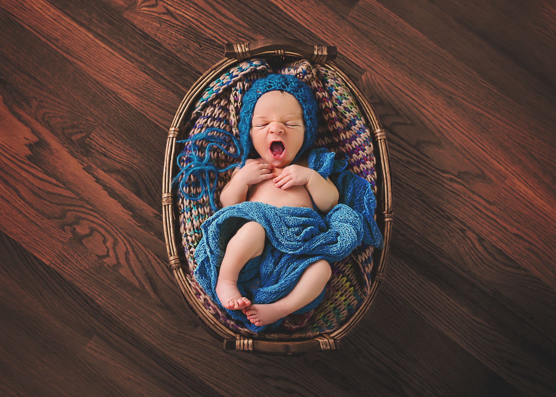 little newborn baby boy yawning in a basket on a dark wood floor