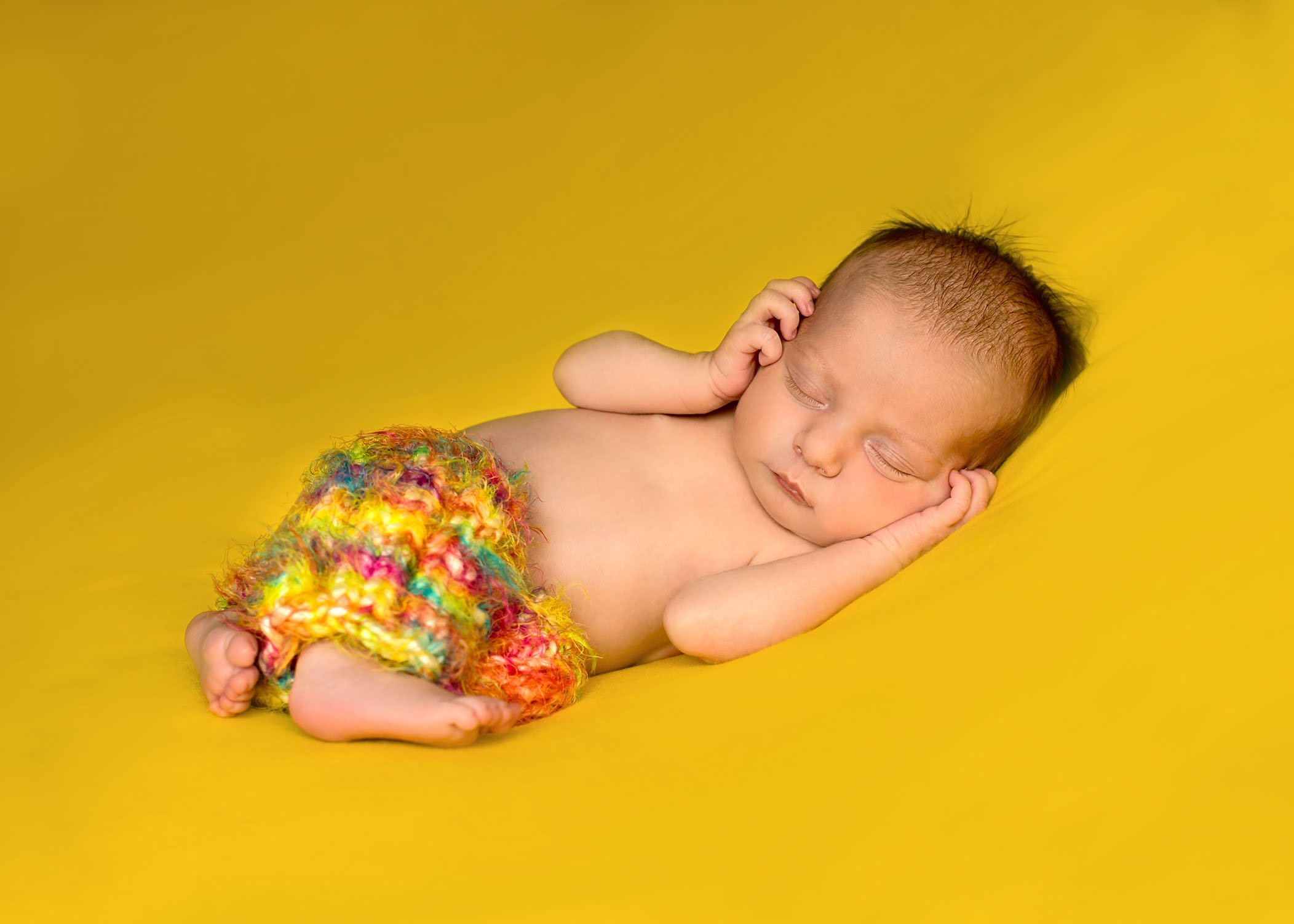 newborn baby girl sleeping on bright yellow backdrop in knitted candy colored pants