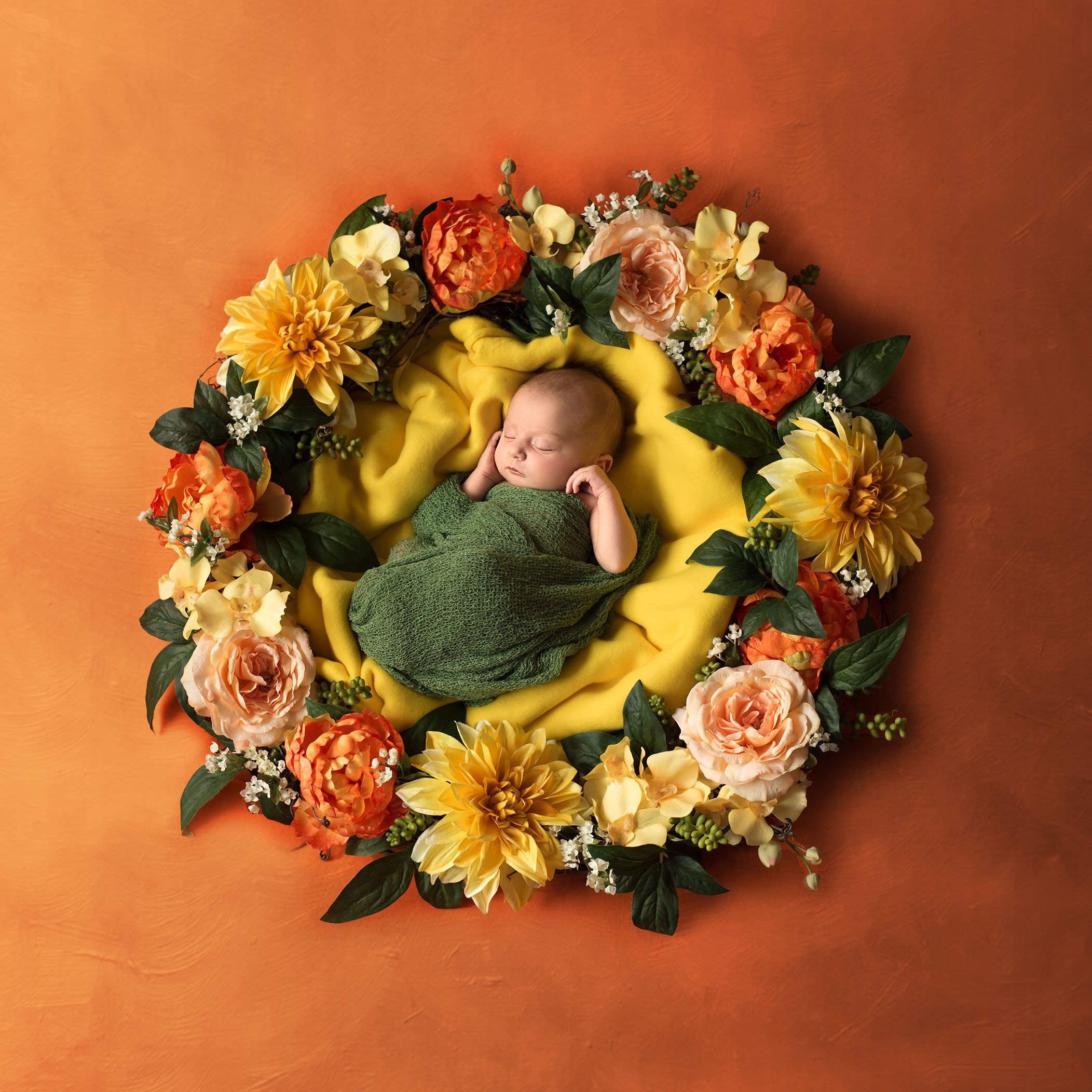newborn baby girl nestled in orange and yellow floral wreath on orange painted backdrop