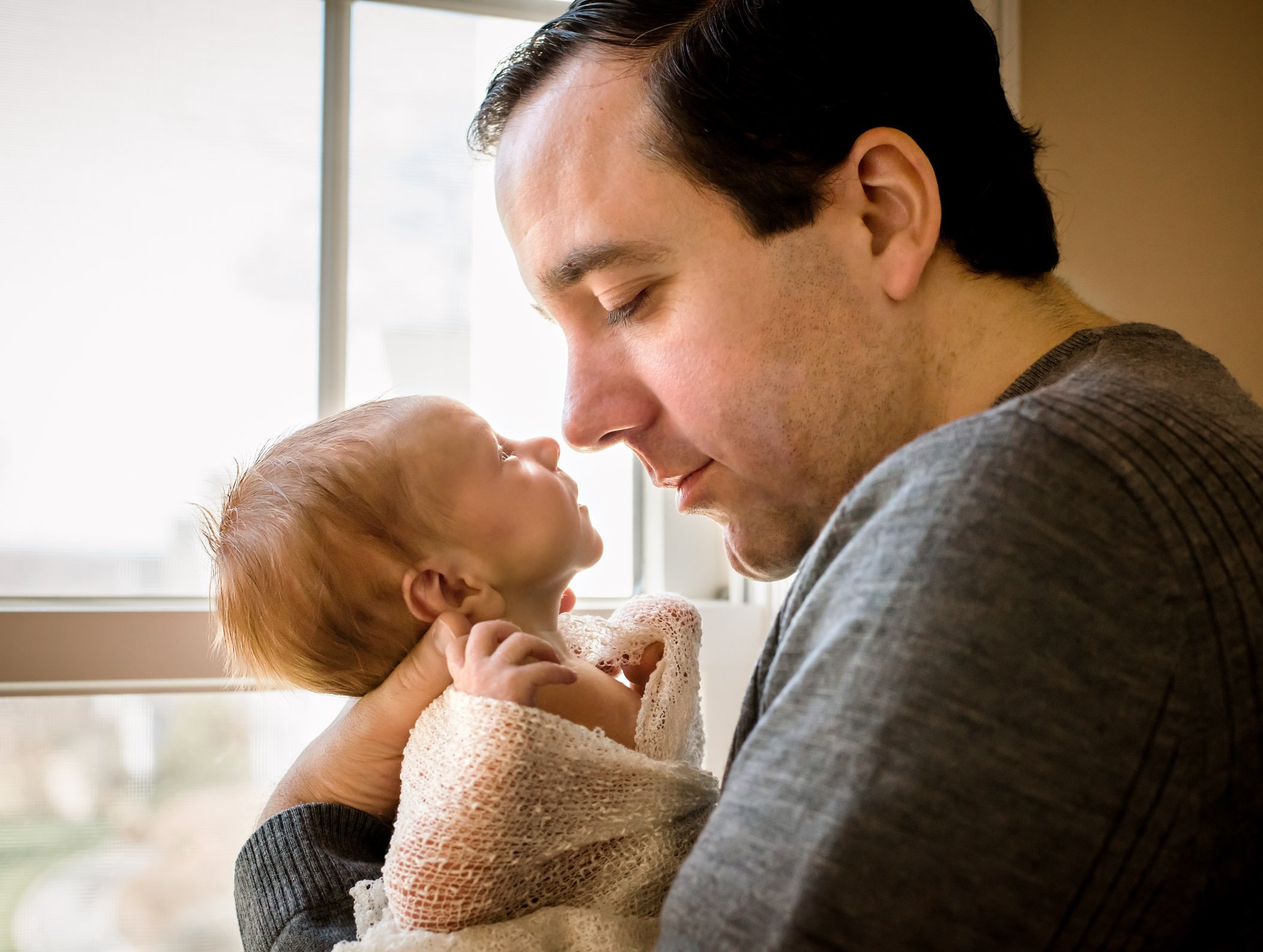 Dad and newborn son nose to nose in the light of the window