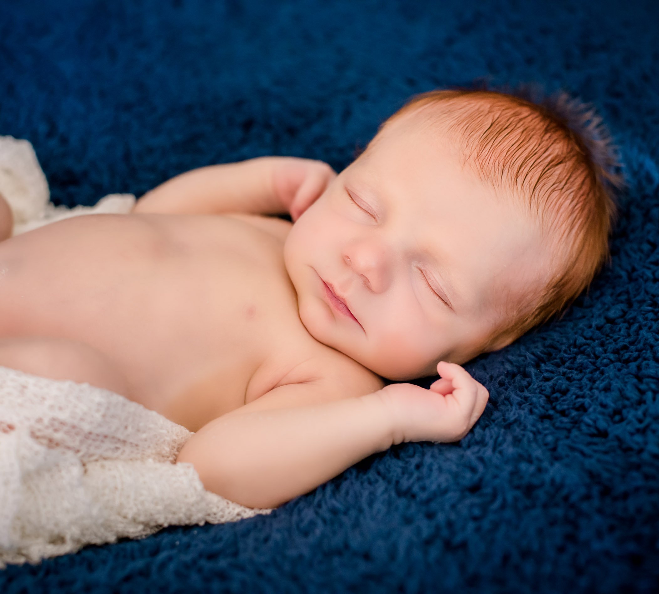 red-headed newborn boy sleeping on back on a blue blanket with white wrapping