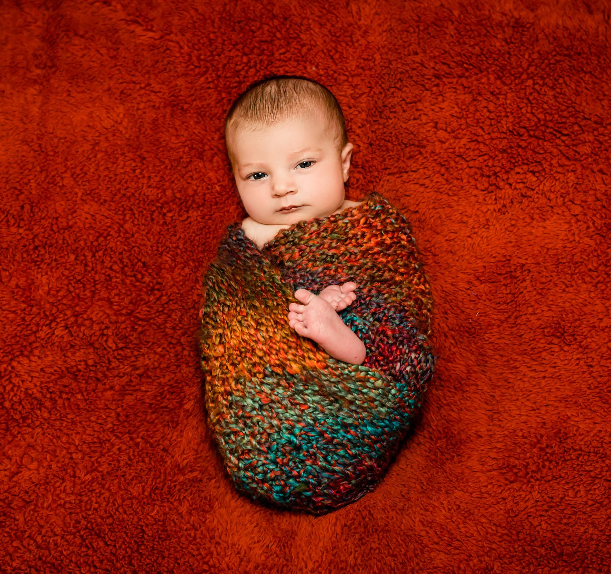 newborn wrapped in a fall-colored knit blanket with just her head and feet visible