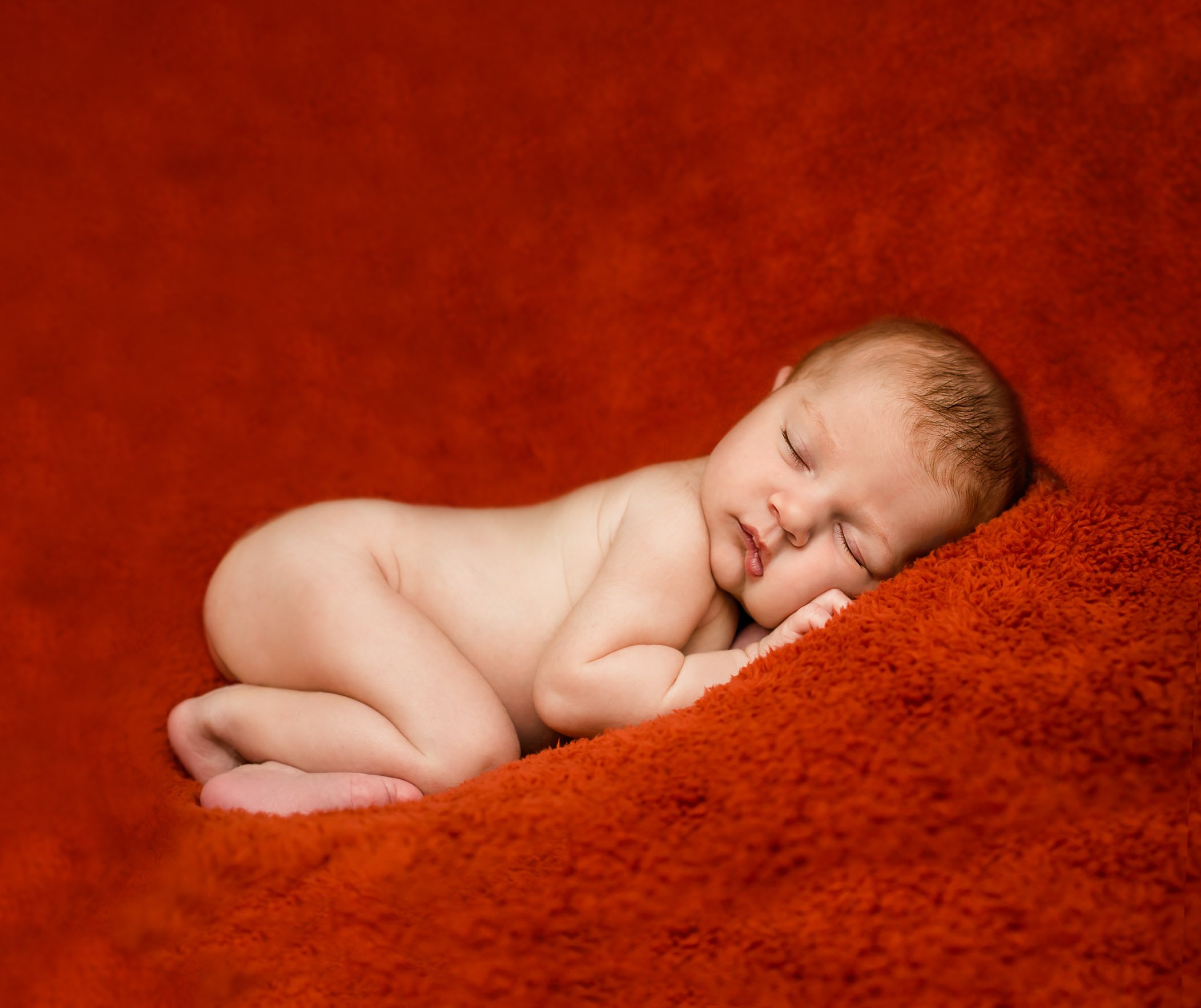 naked newborn baby sleeping on a rust colored blanket