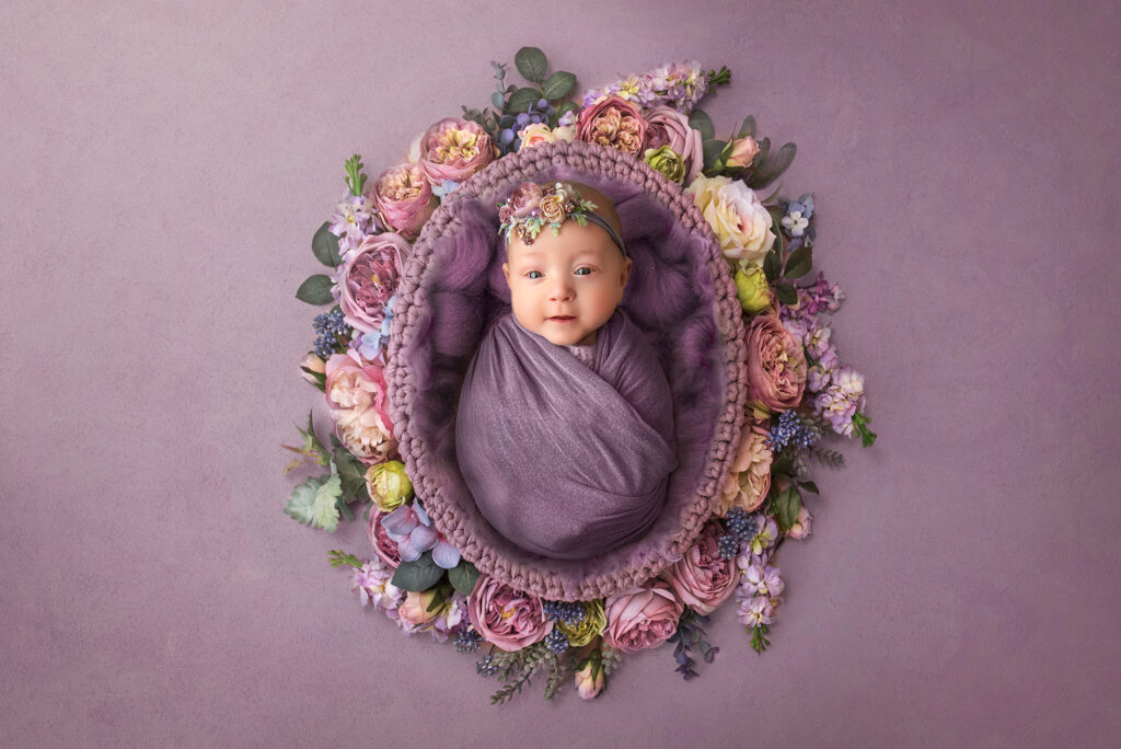 best time for newborn photoshoot baby girl resting in ring of purple flowers
