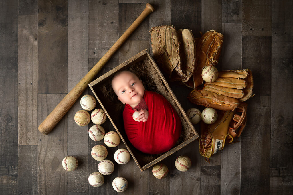 best time to take newborn photos baby boy sleeping in crate surrounded by baseball gear