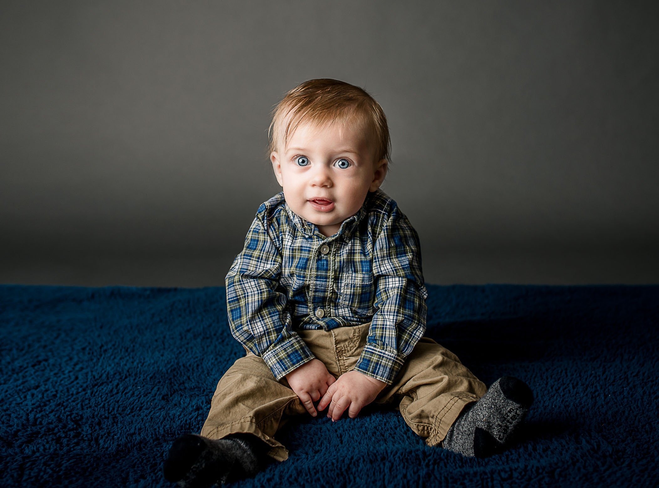 blue eyed 6 month old baby boy sitting up on blue rug