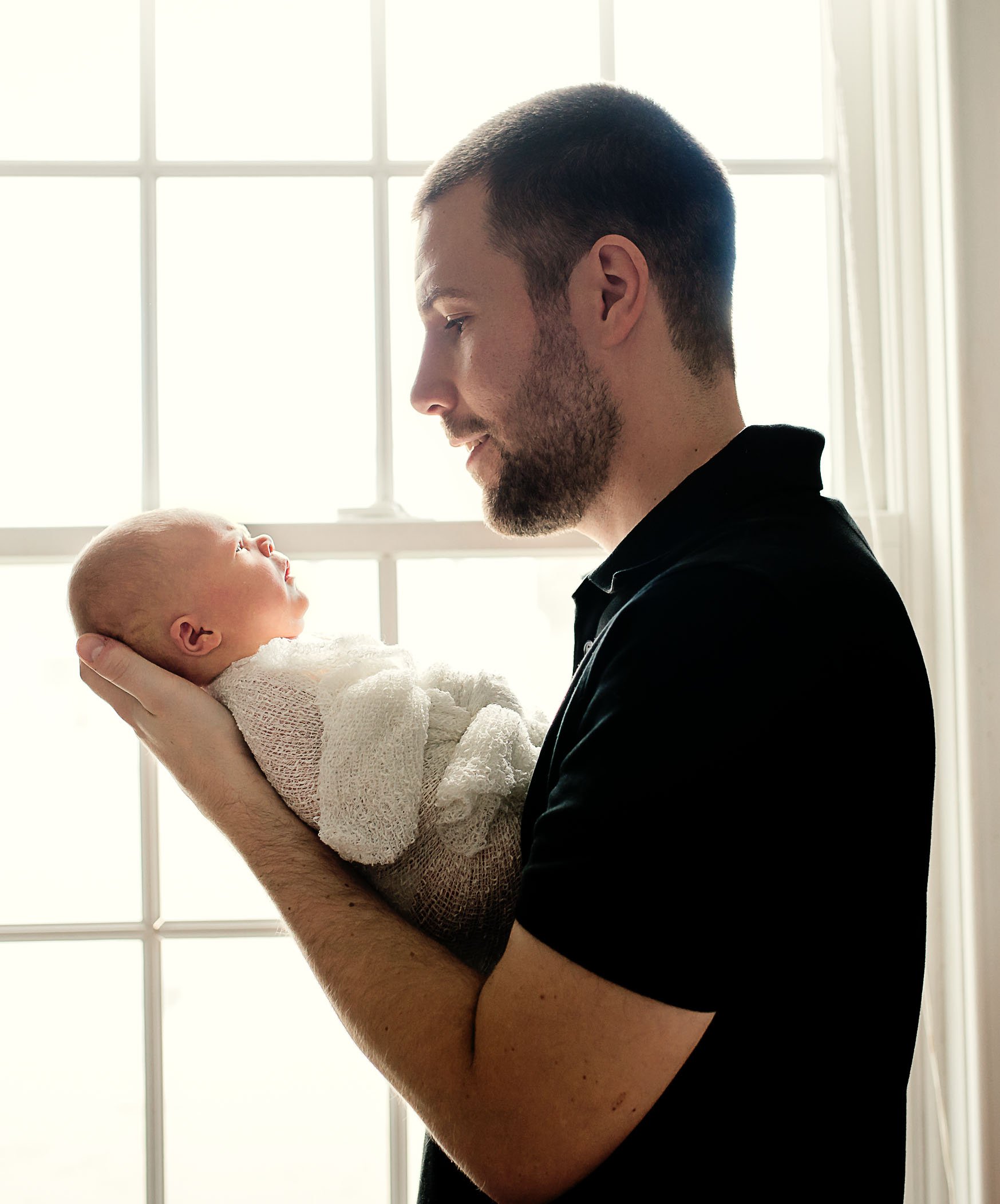 new Dad holding his newborn daughter in the window light